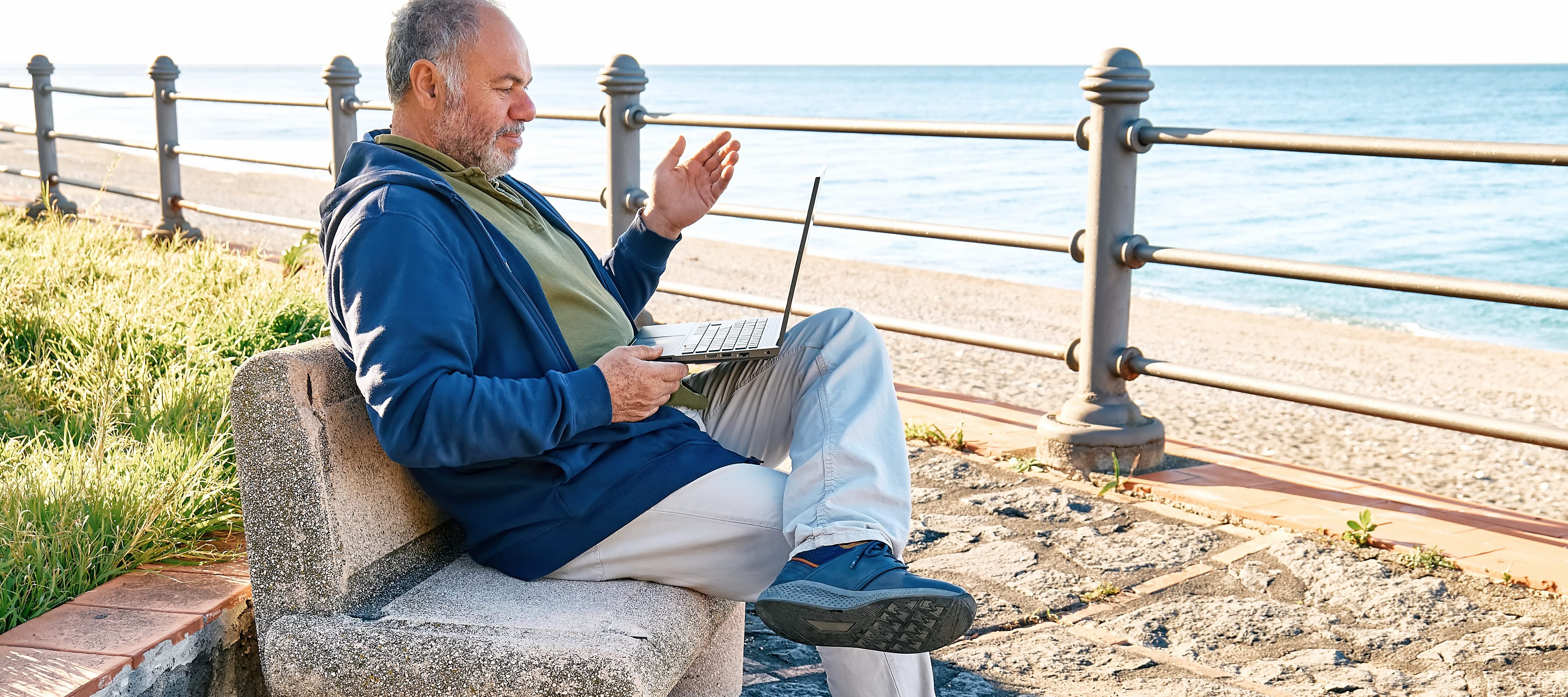Older man using laptop on park bench, reviewing his finances.