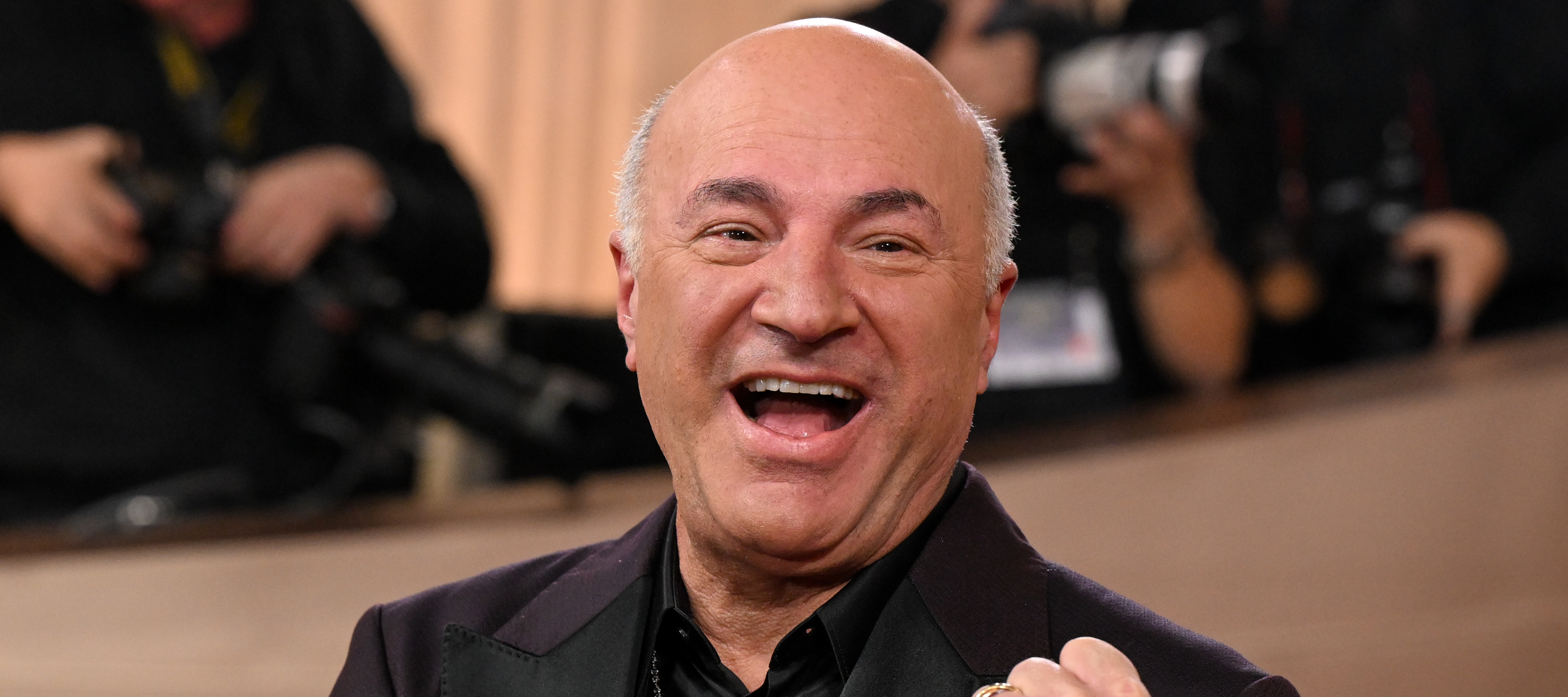 Shark Tank investor Kevin O'Leary poses with both fists raised, smiling.