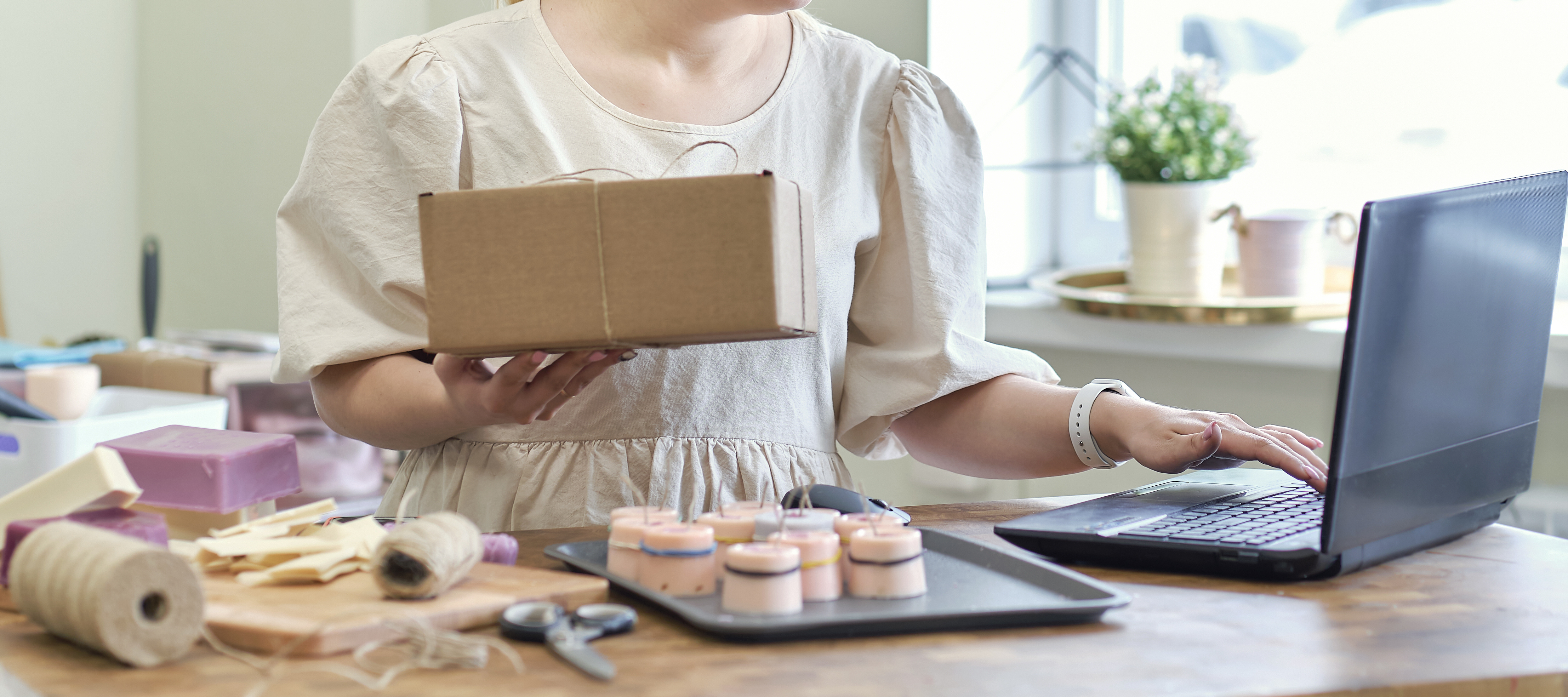 A woman holding a package while conducting business on her laptop in a shop.