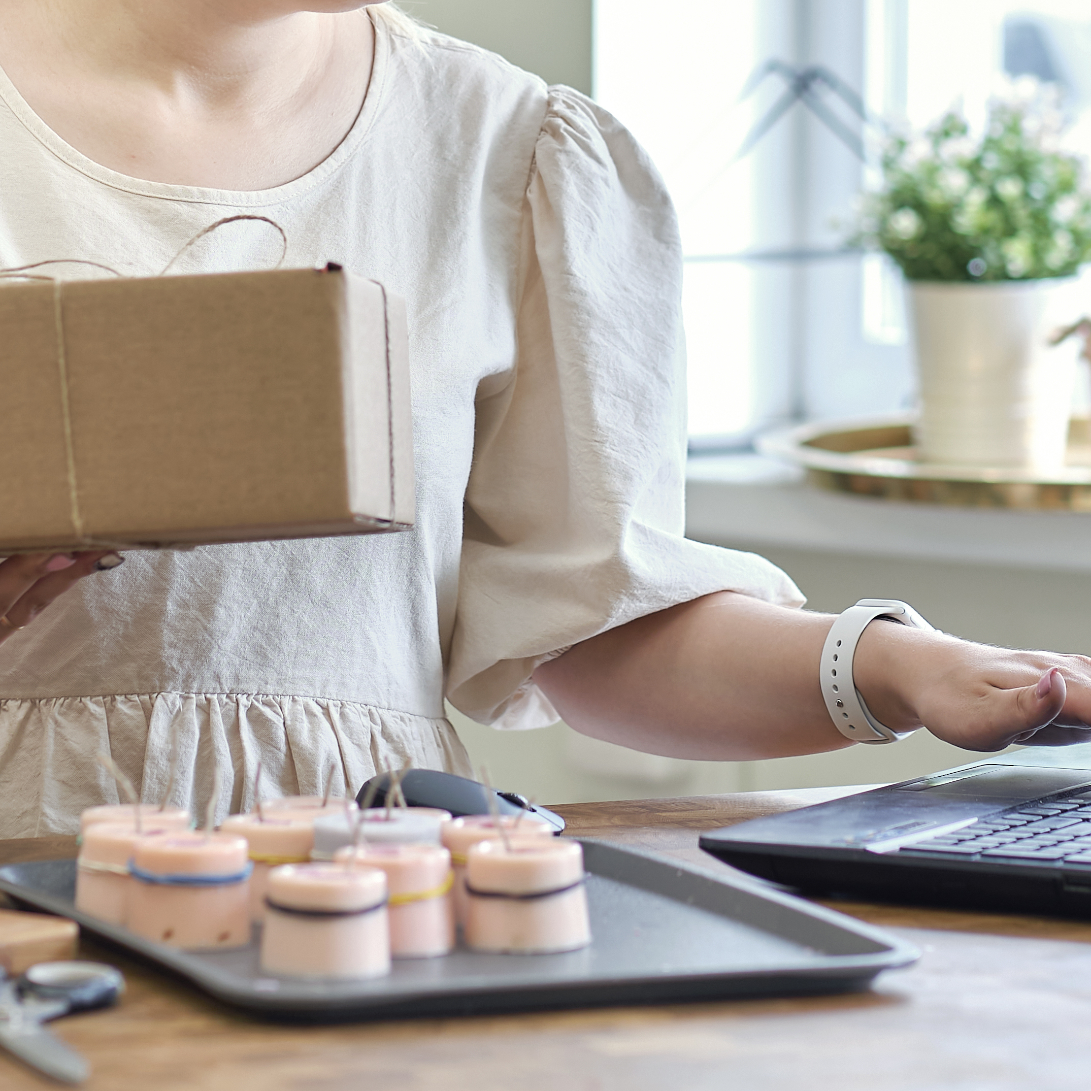 A woman holding a package while conducting business on her laptop in a shop.