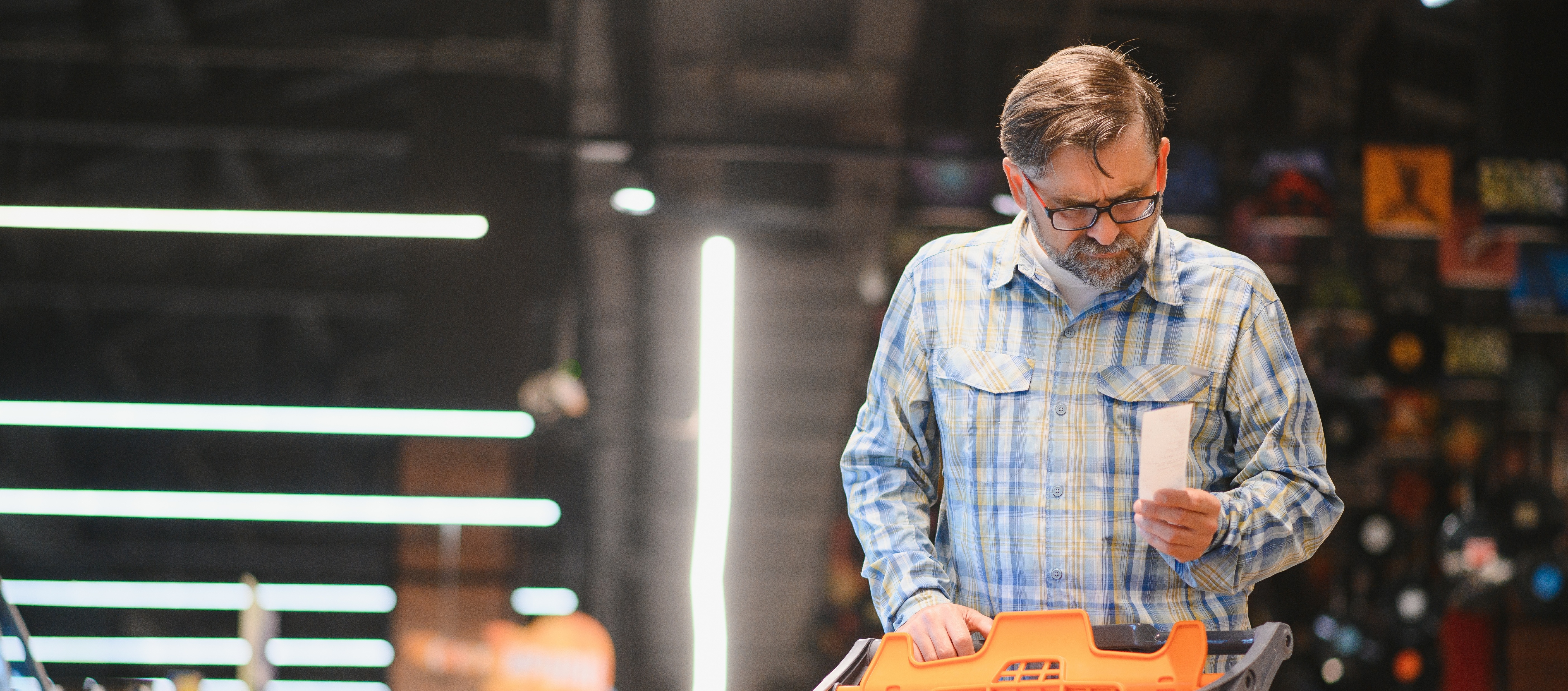 A middle-aged man stares intently at a recept while grocery shopping.