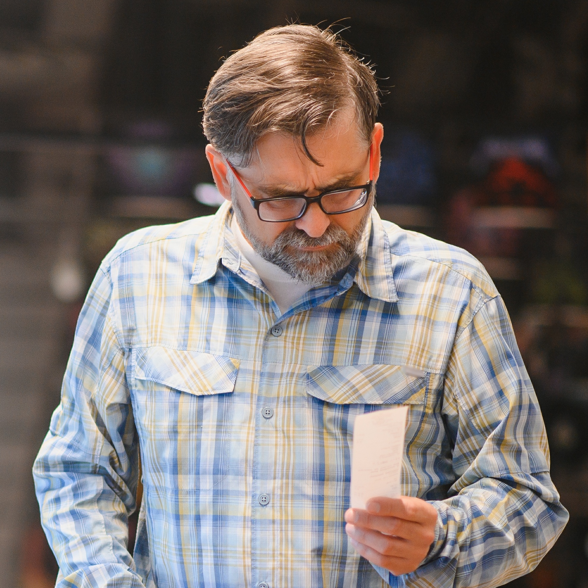 A middle-aged man stares intently at a recept while grocery shopping.
