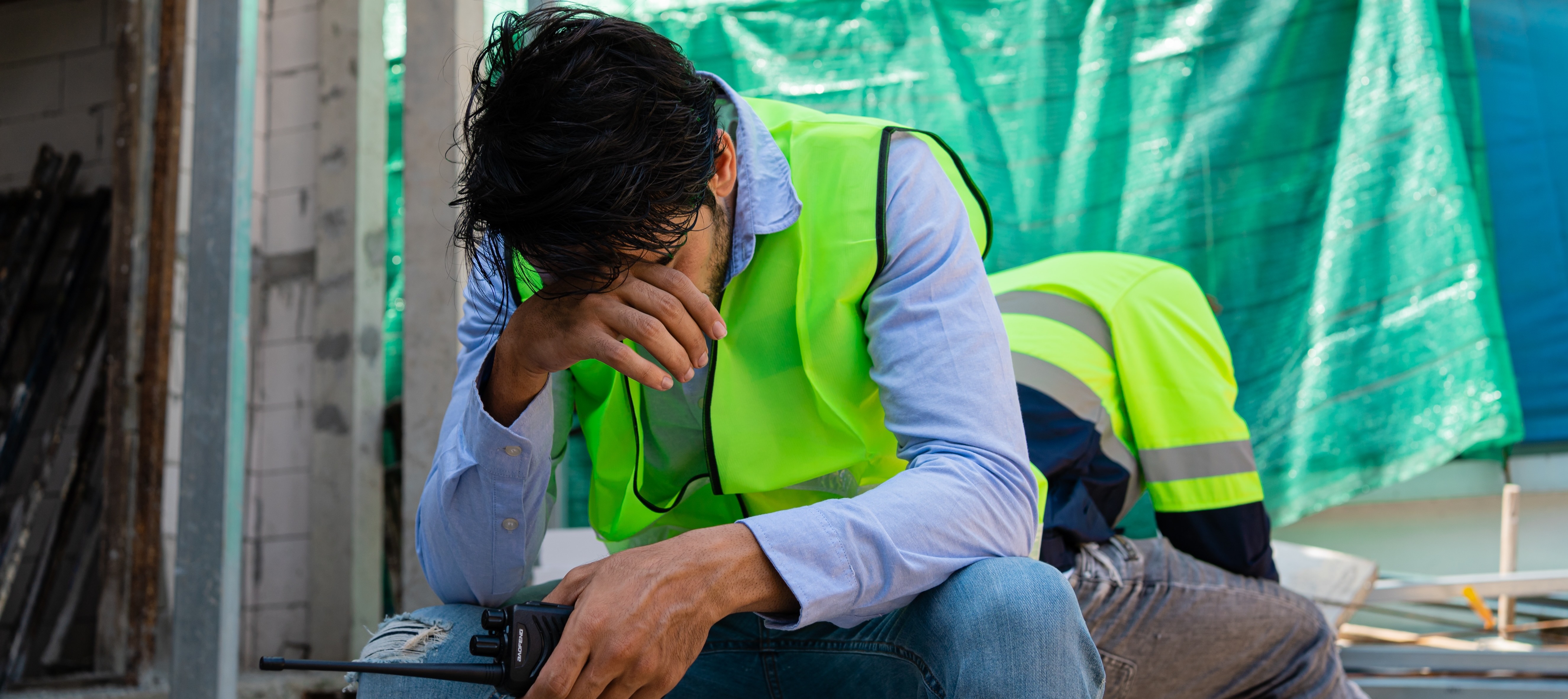 A man sits with his hand in his face while on a construction site.