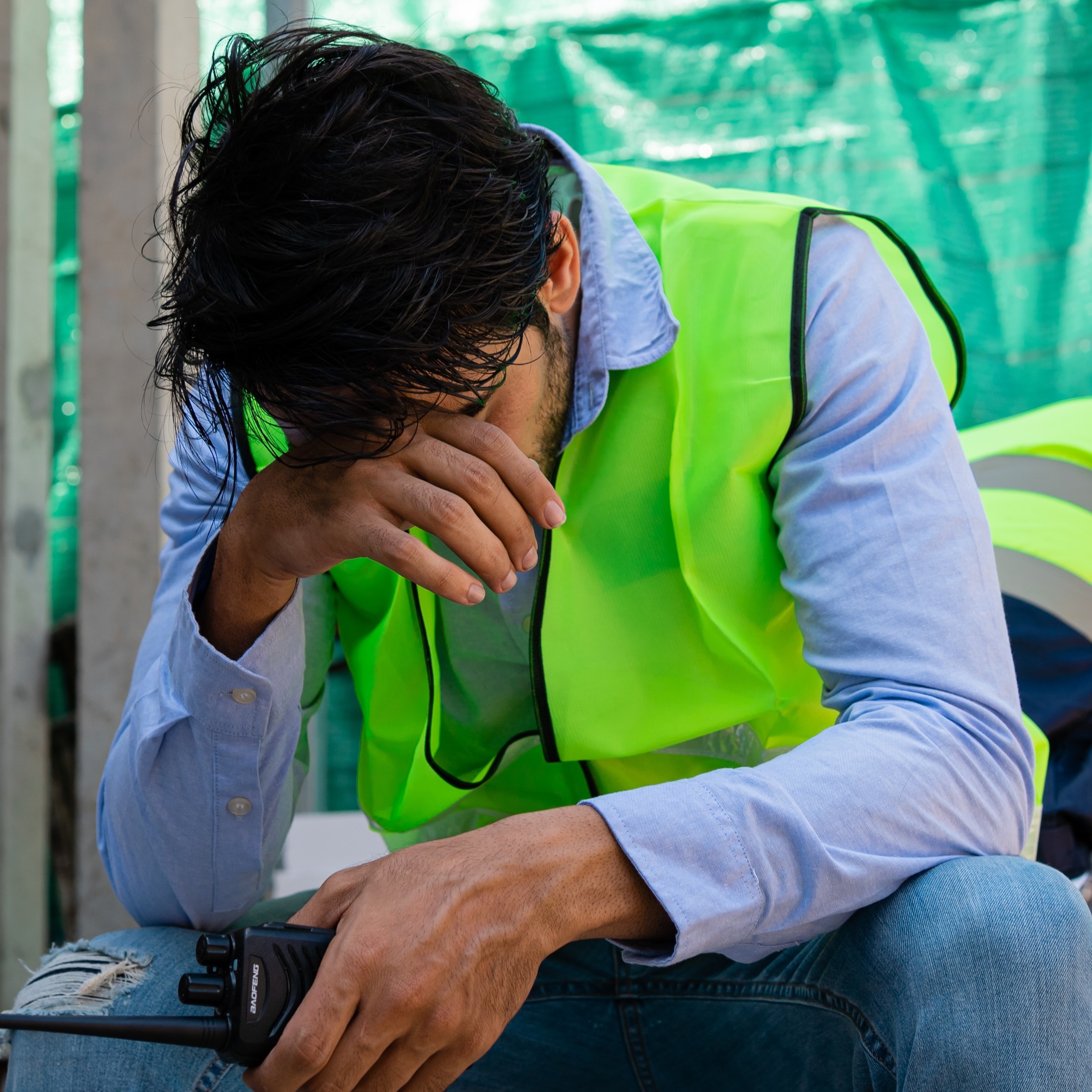 A man sits with his hand in his face while on a construction site.