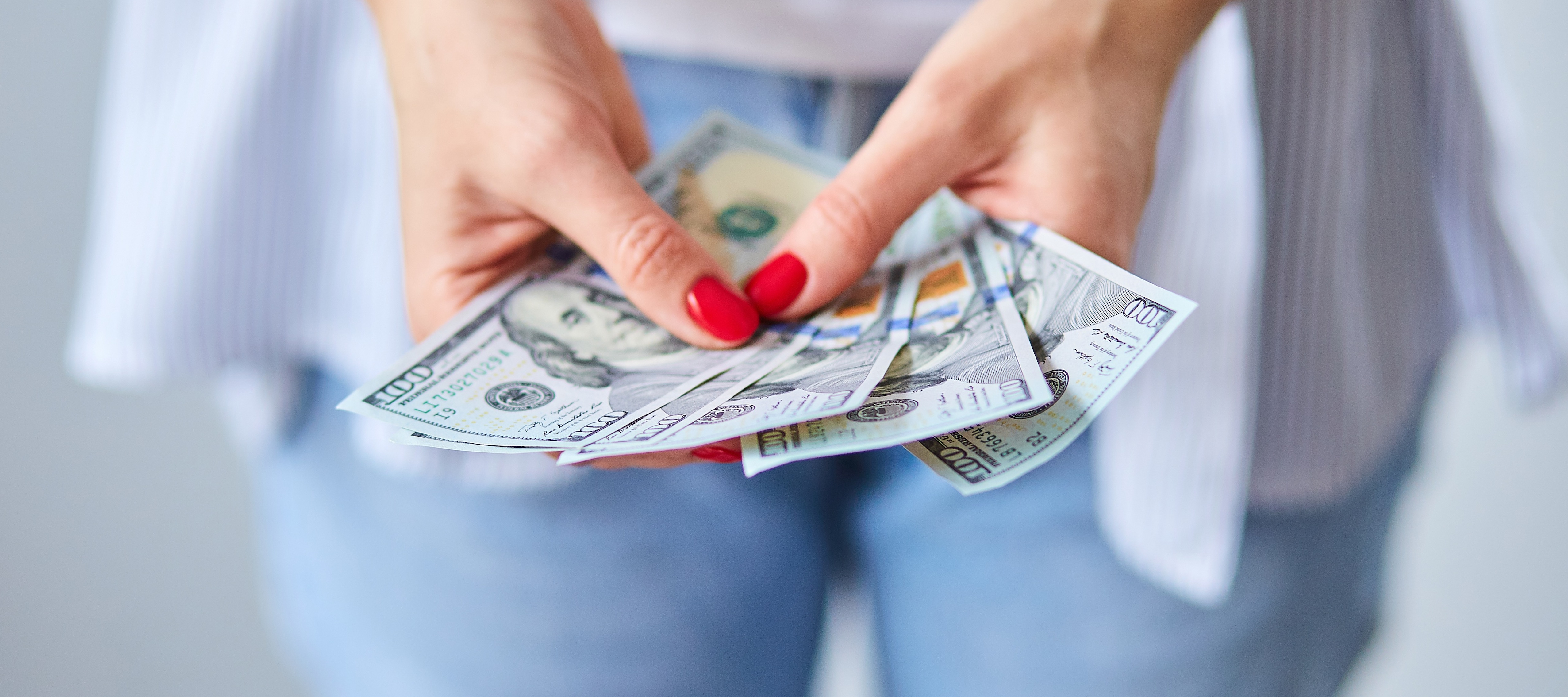 Close up of a woman holding a handful of hundred dollar bills.