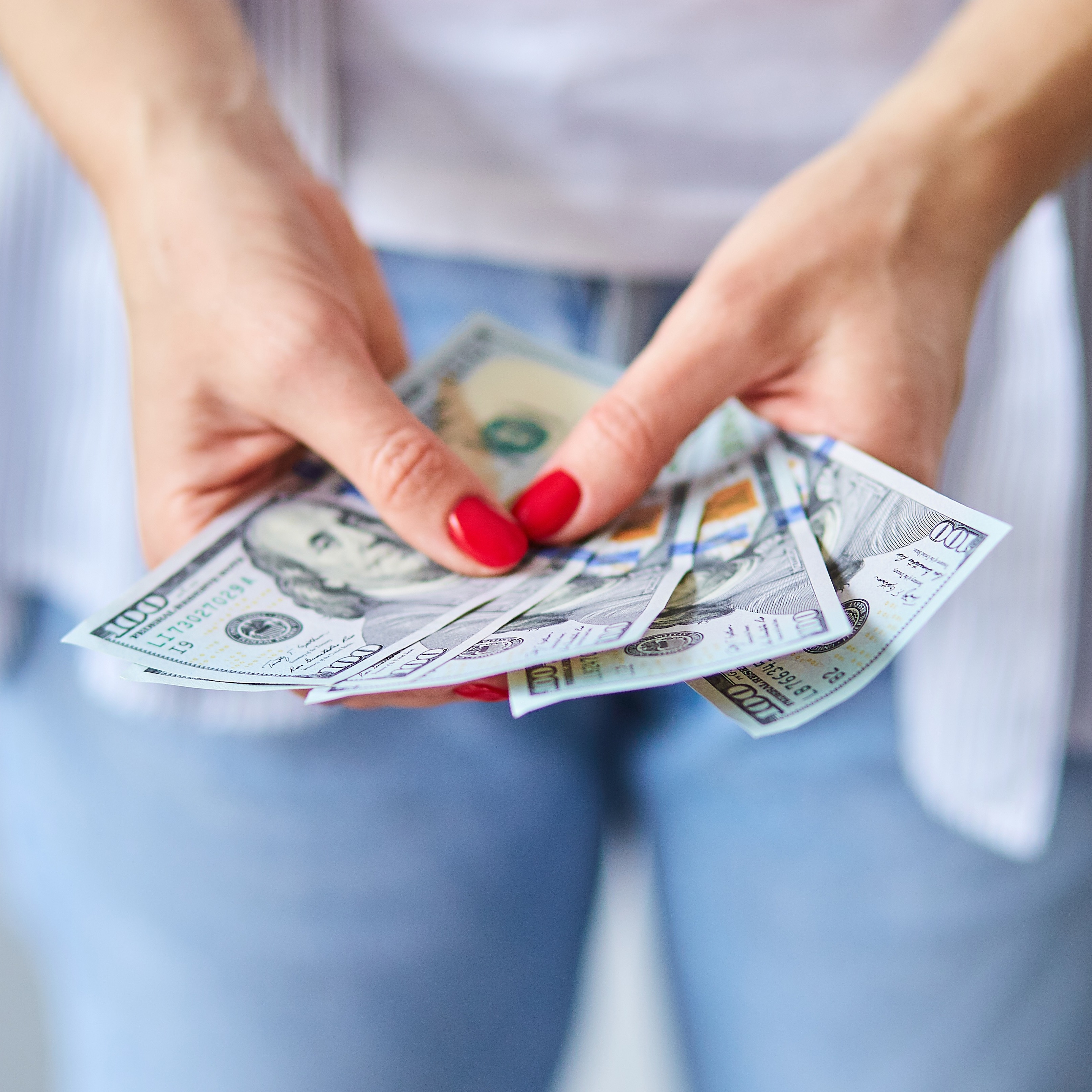 Close up of a woman holding a handful of hundred dollar bills.