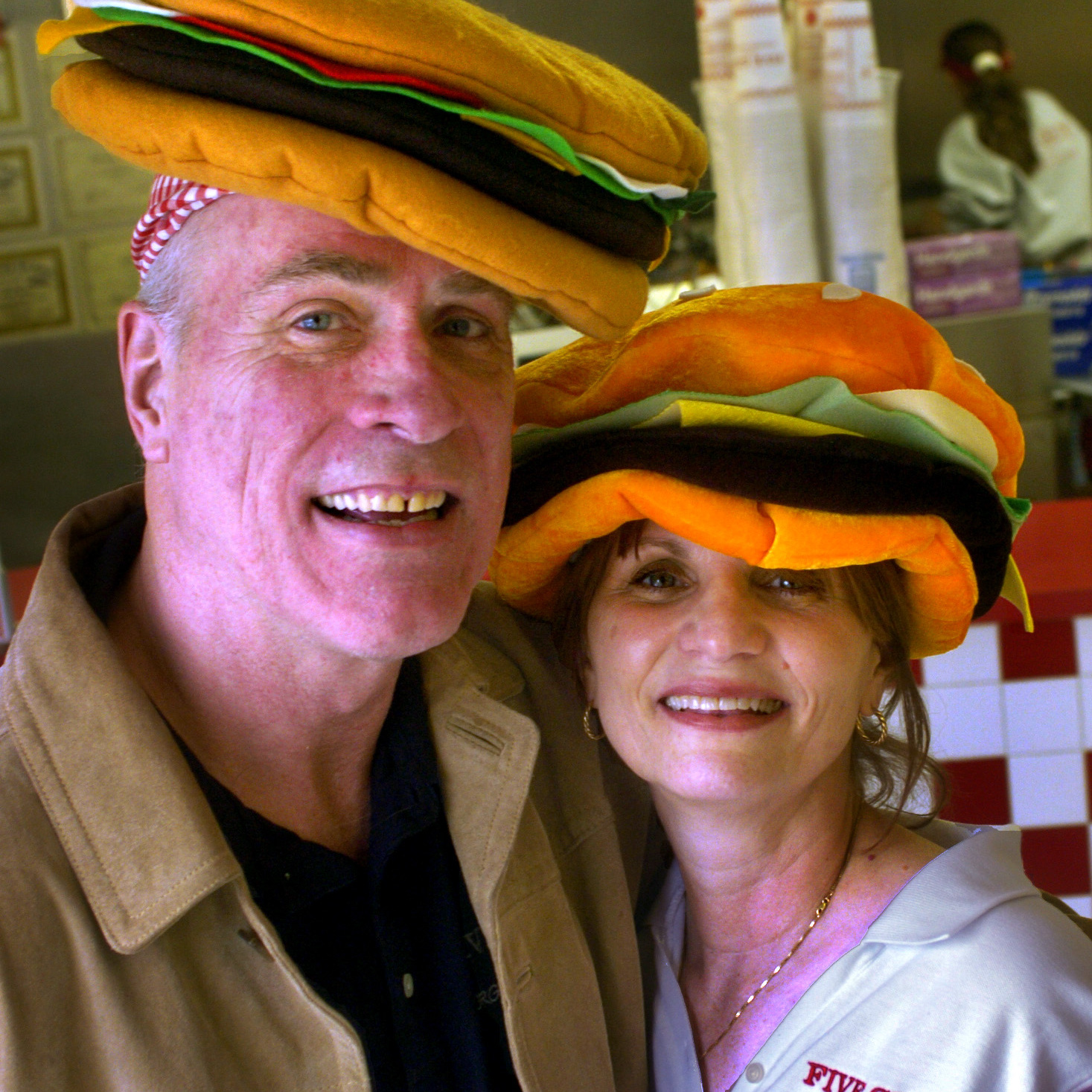Jerry and Janie Murrell smile while wearing hamburger shaped hates inside of a Five Guys restaurant.