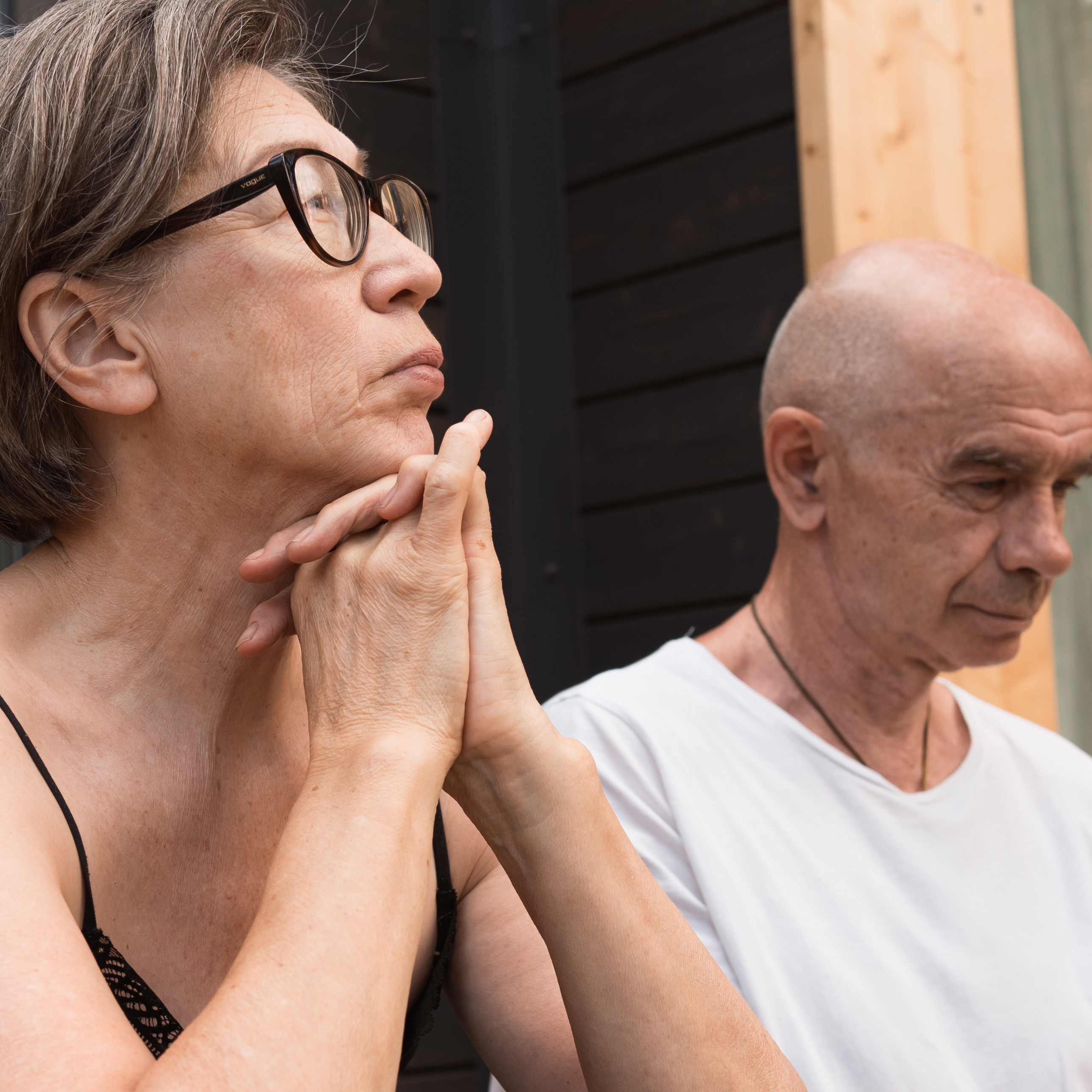 Middle aged woman pensively resting chin on hands while sitting next to middle aged man.