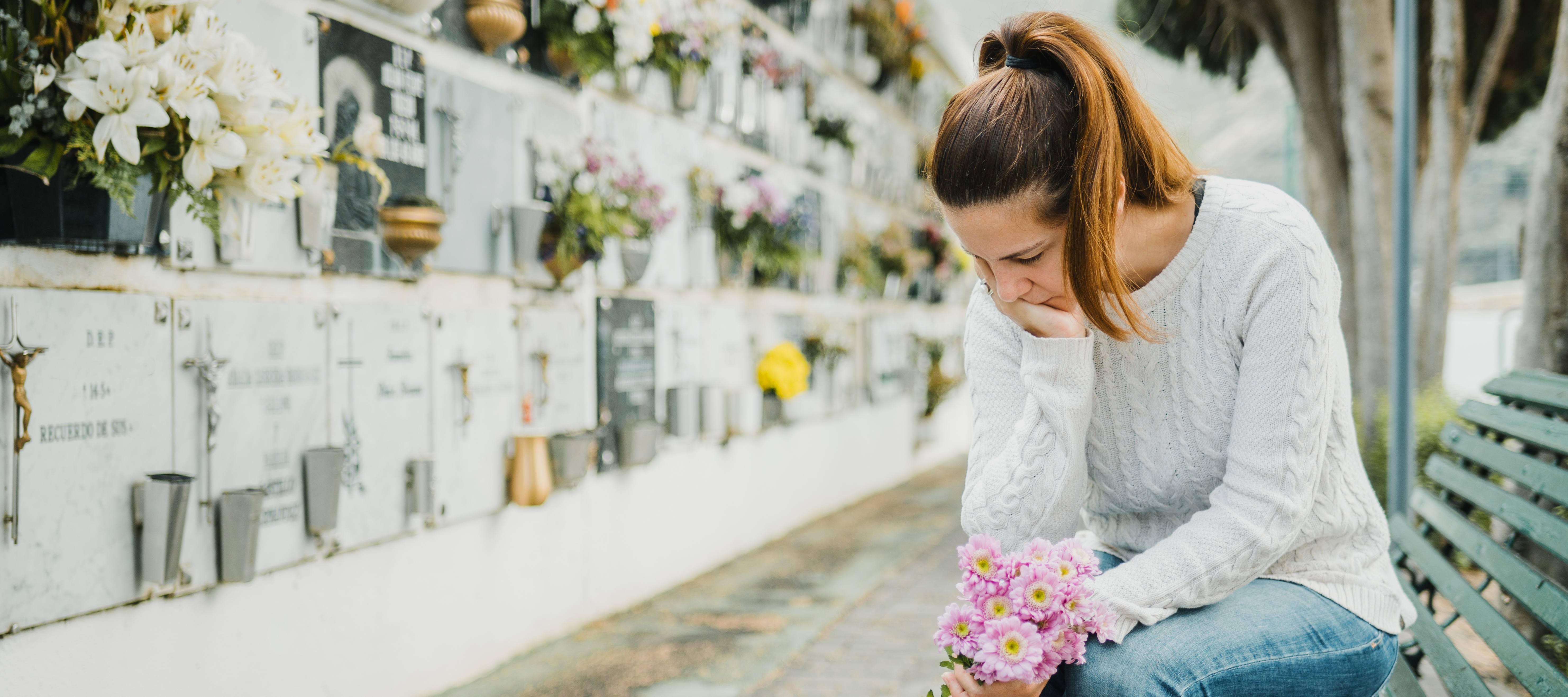 A woman sits in front of a row of tombs, holding a bouquet of flowers.