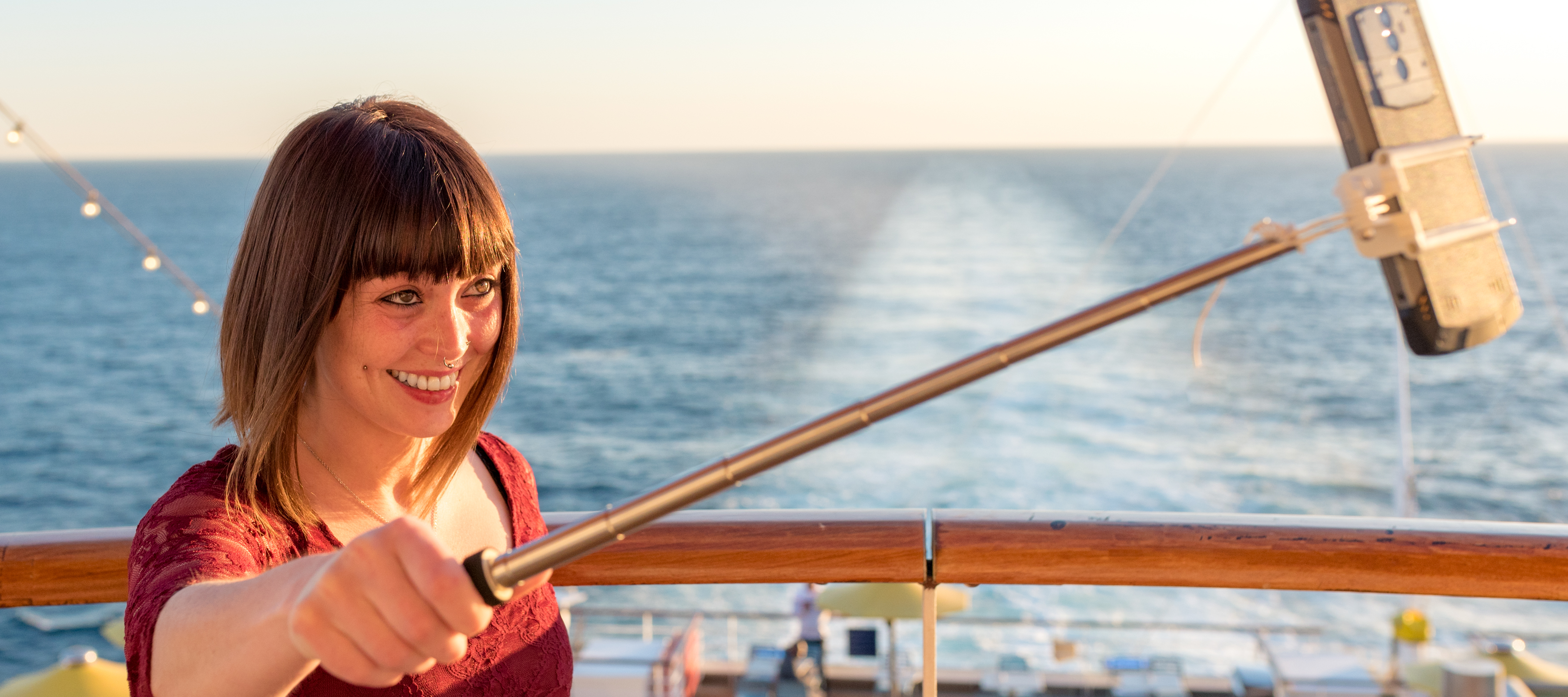 A smiling young woman taking a selfie with a selfie stick on a cruise ship.