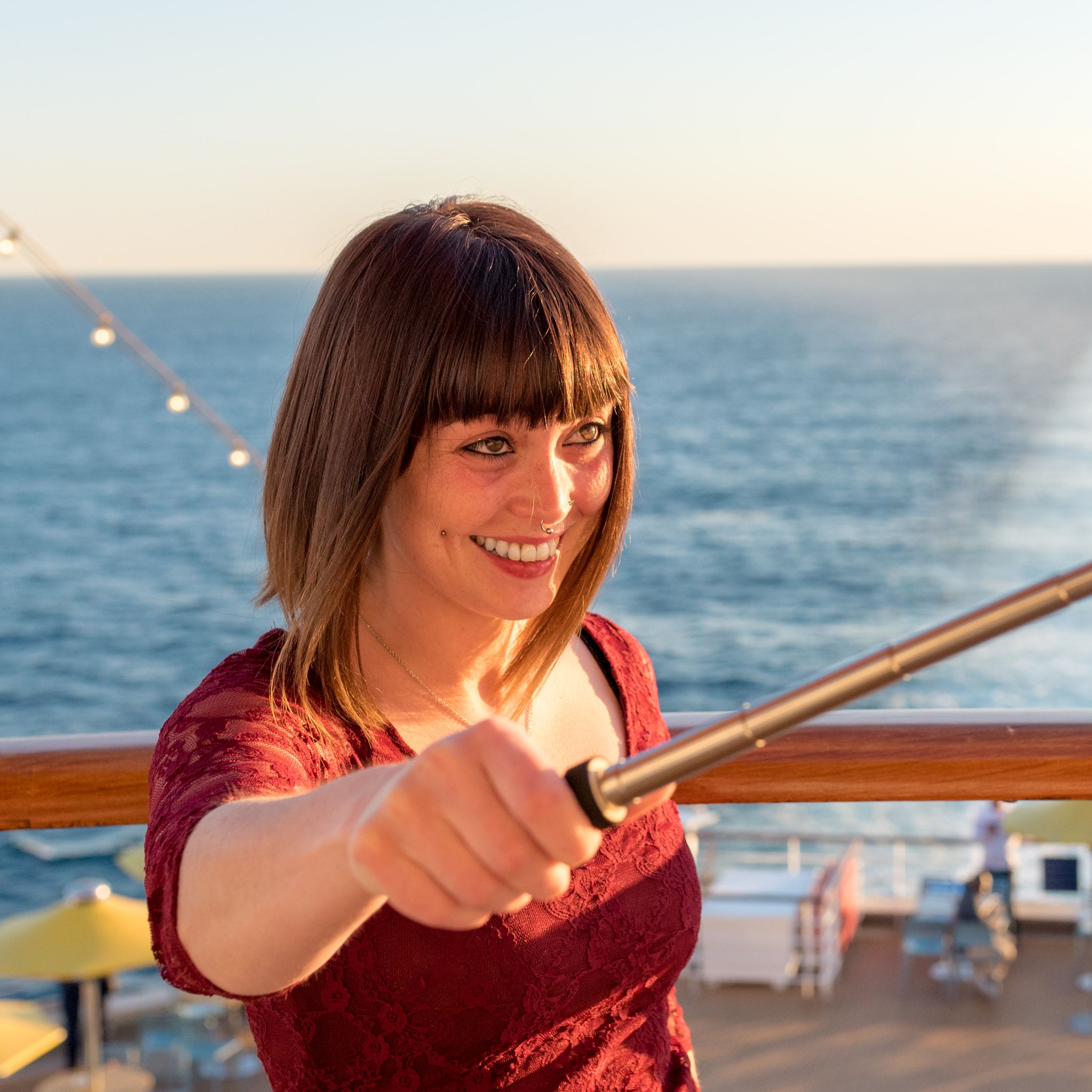 A smiling young woman taking a selfie with a selfie stick on a cruise ship.