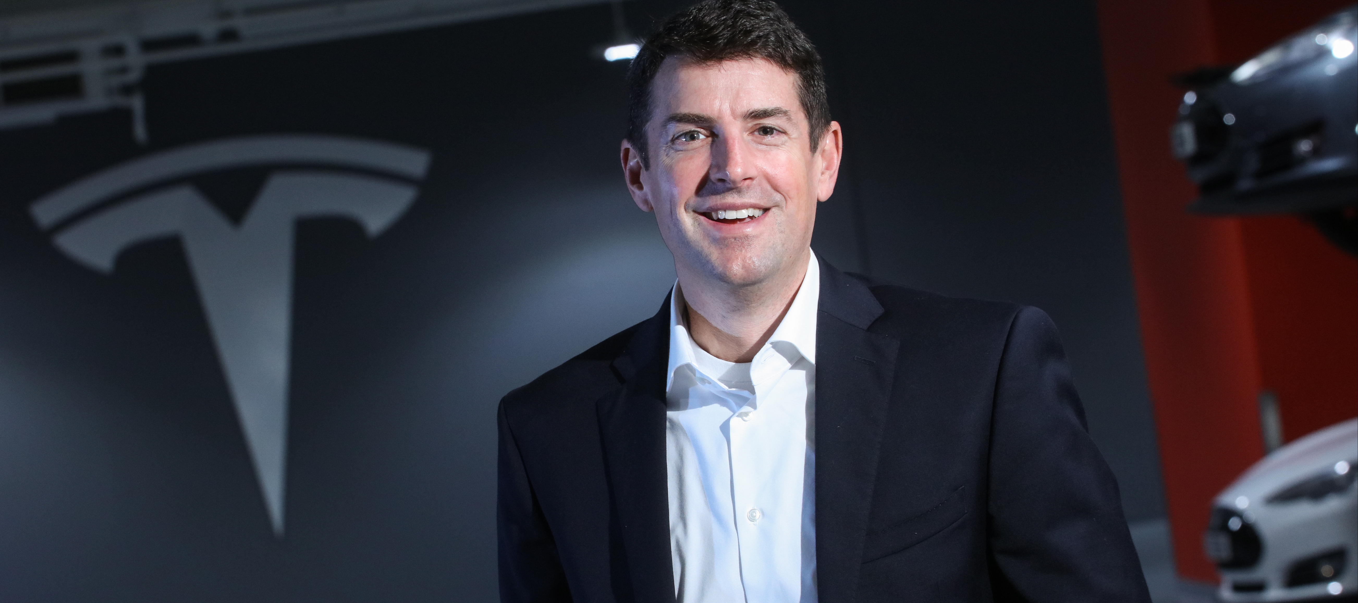 Jon McNeill poses in front of Tesla logo