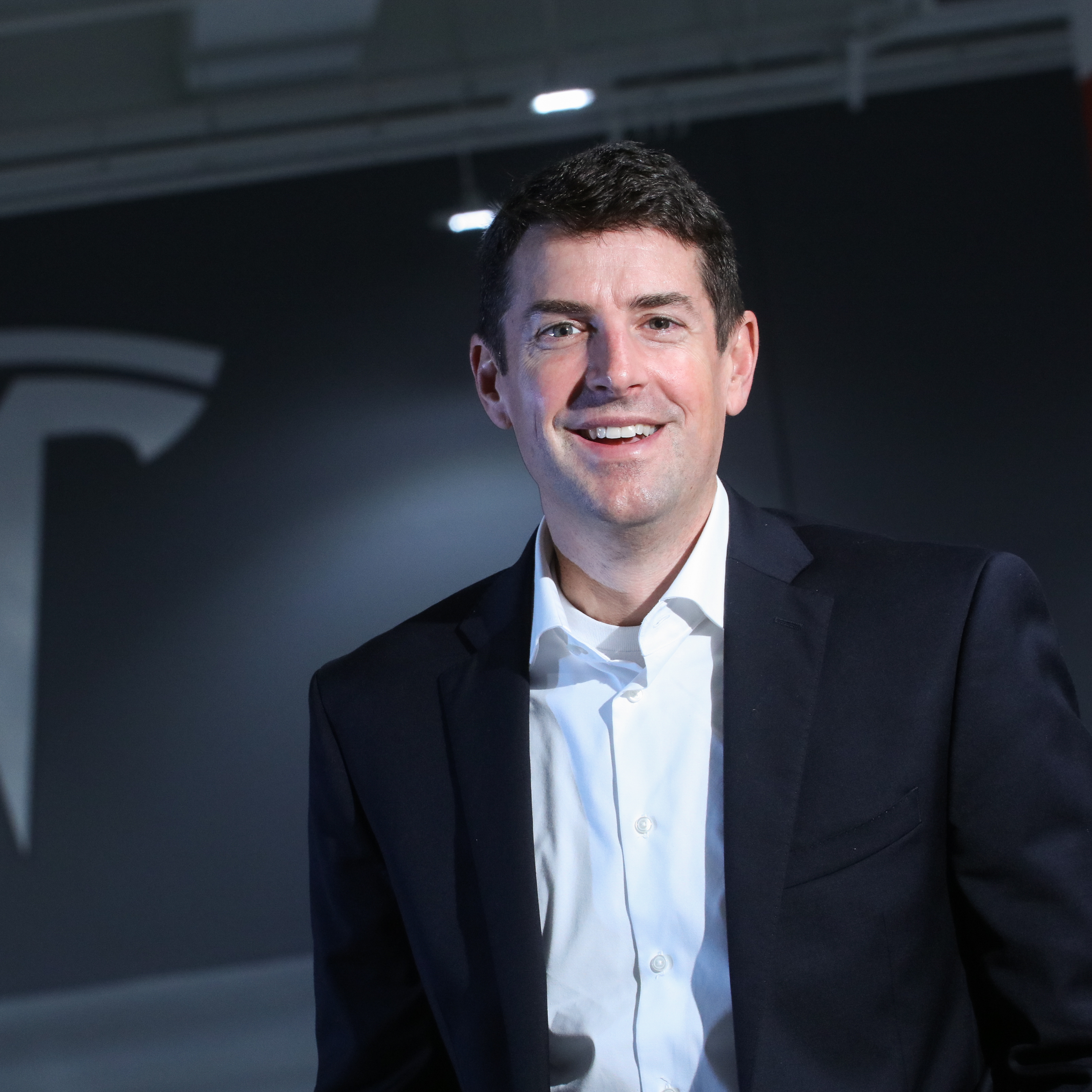 Jon McNeill poses in front of Tesla logo