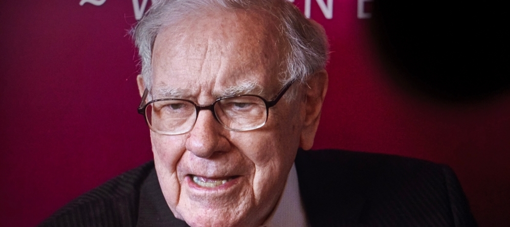 A photo of Warren Buffett speaking against a red backdrop.