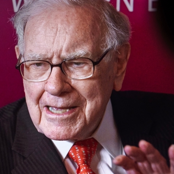 A photo of Warren Buffett speaking against a red backdrop.