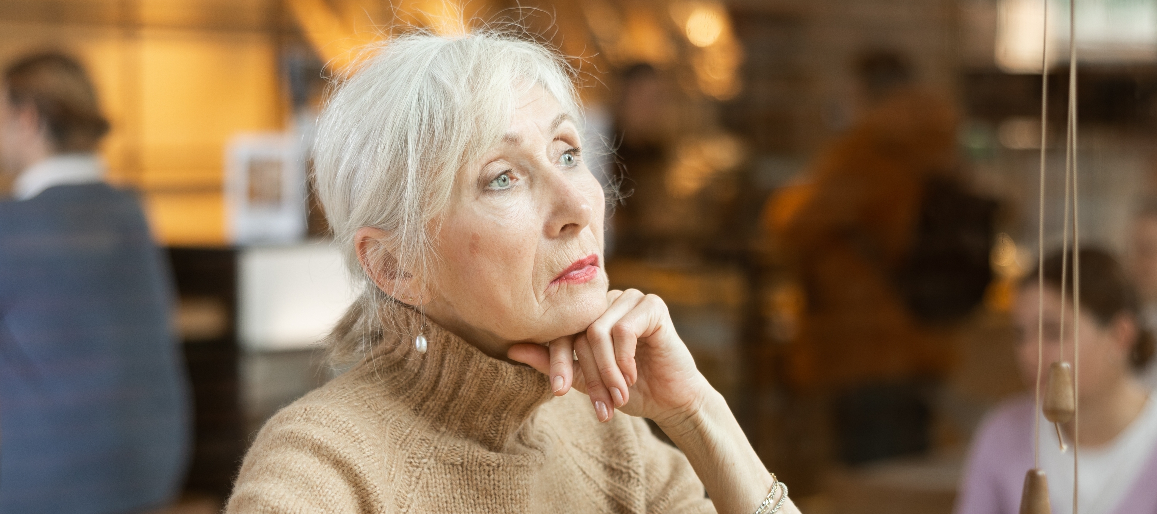 A well dressed woman looks into the middle distance, nursing a cup of coffee.