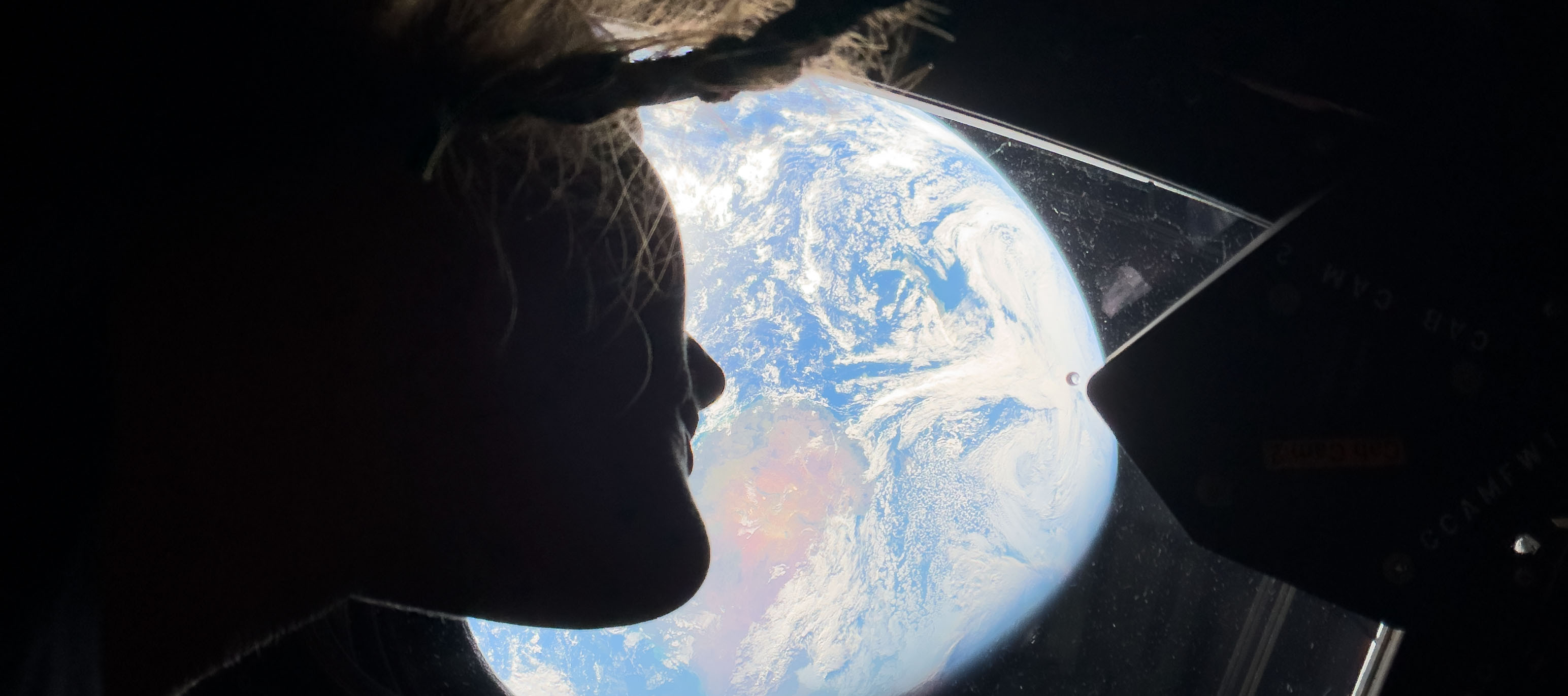 NASA astronaut and Artemis II mission specialist Christina Koch peers out of one of the Orion spacecraft's main cabin windows.