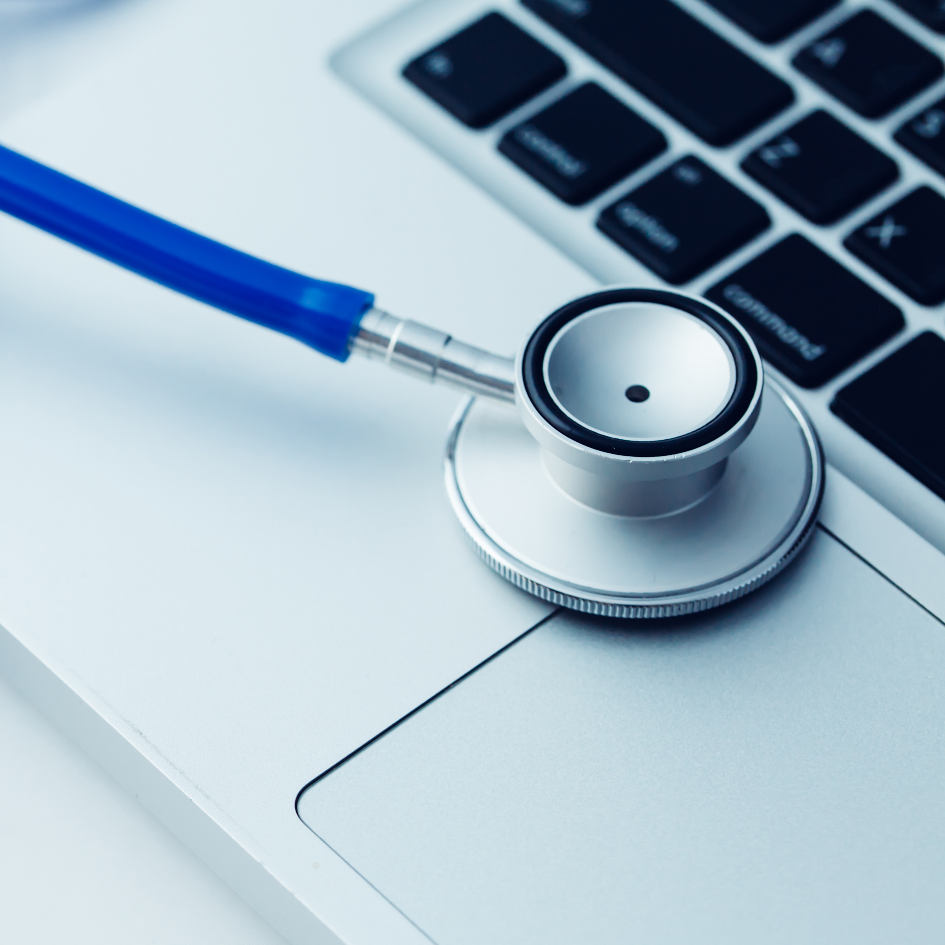 A close-up shot features a blue stethoscope placed on a silver laptop.