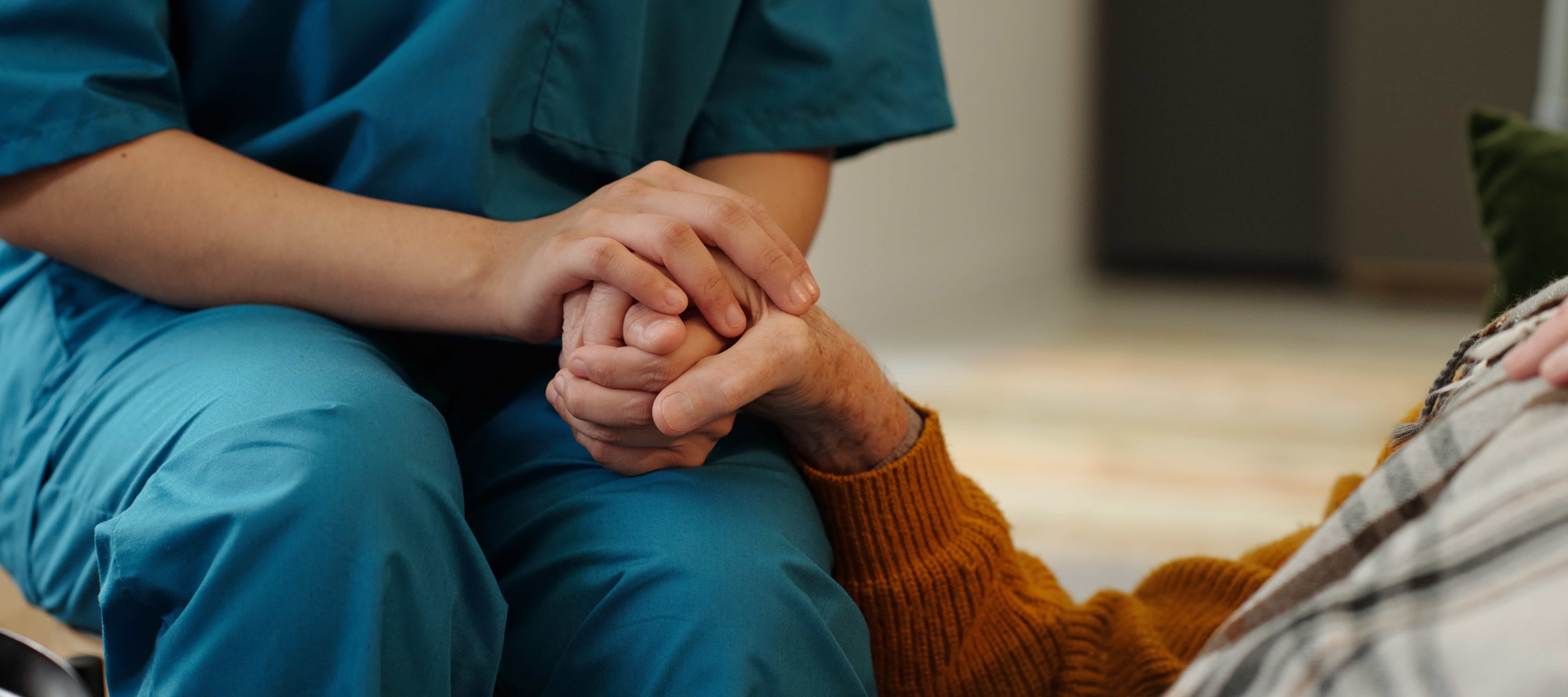 A health care worker holding a patient's hand in hospice