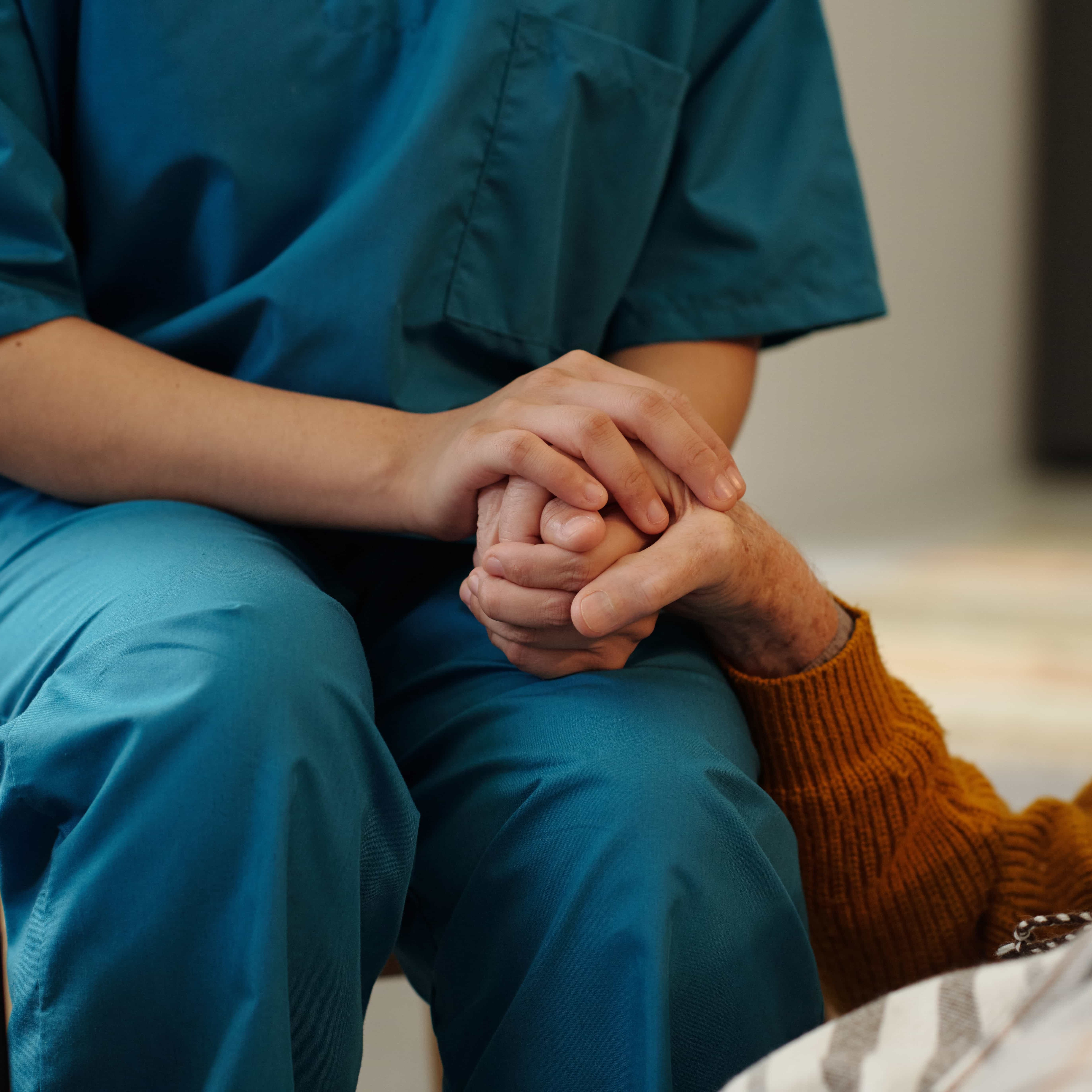 A health care worker holding a patient's hand in hospice