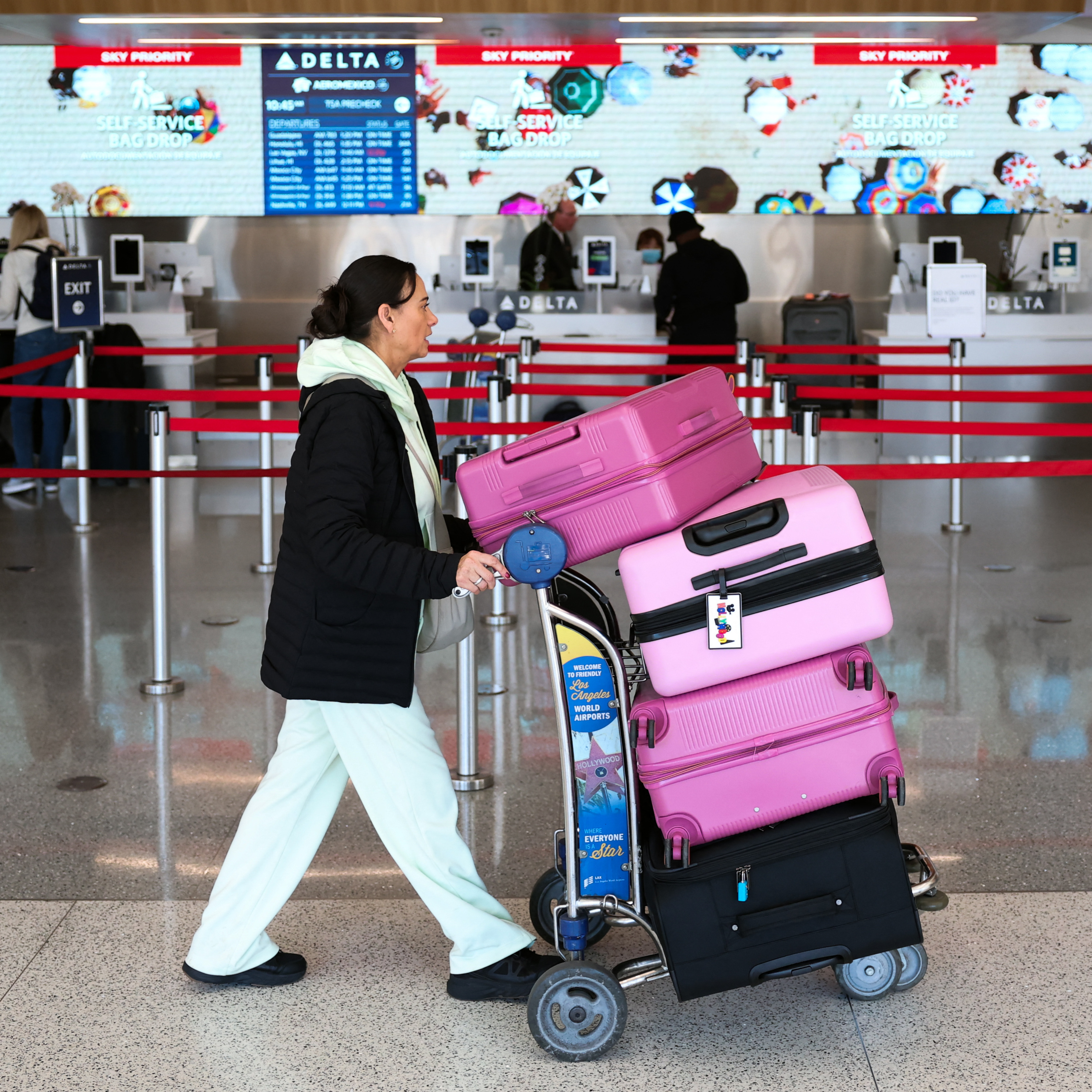 A passenger pushes a baggage cart loaded with suitcases past a Delta Air Lines check-in counter at Los Angeles International Airport (LAX) in Los Angeles, on November 26, 2025.