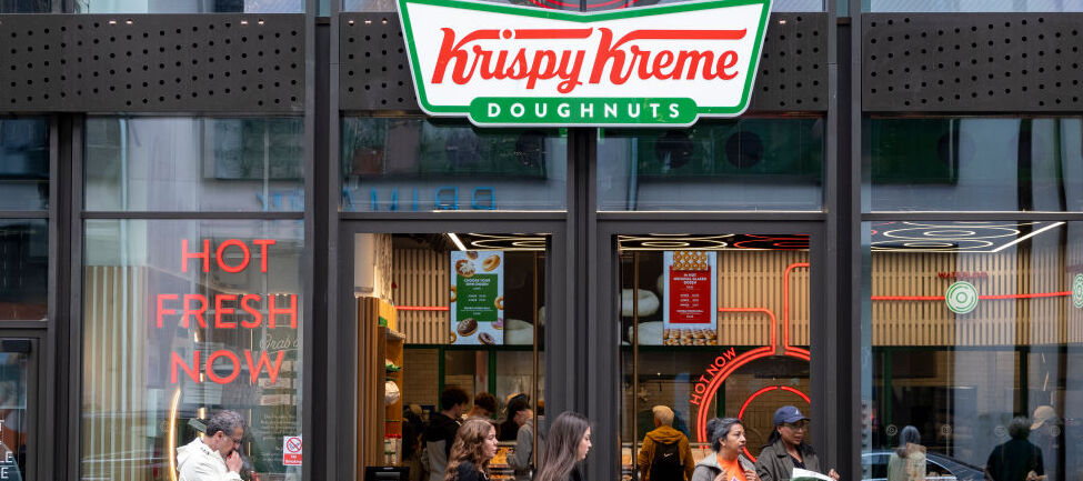 People walking on the sidewalk past a Krispy Kreme location