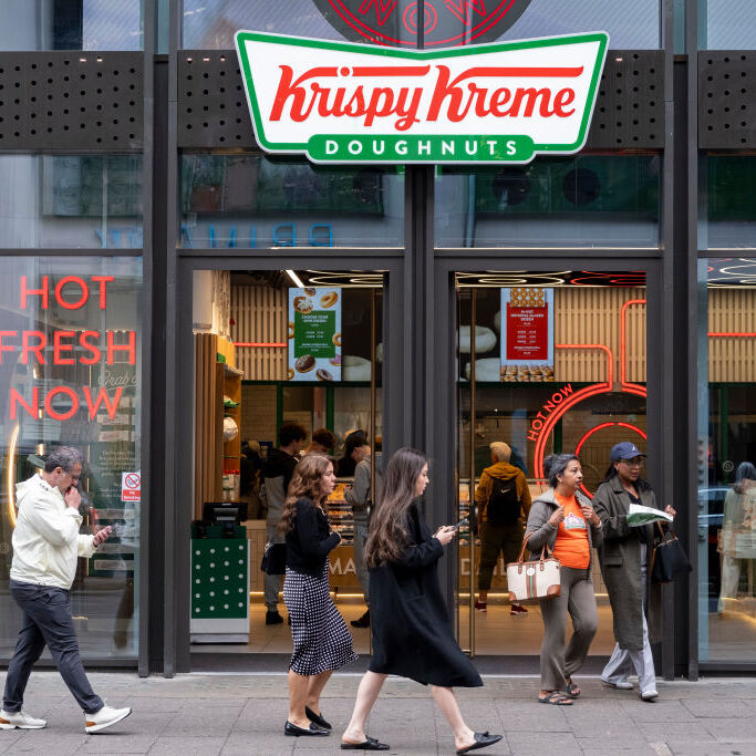 People walking on the sidewalk past a Krispy Kreme location