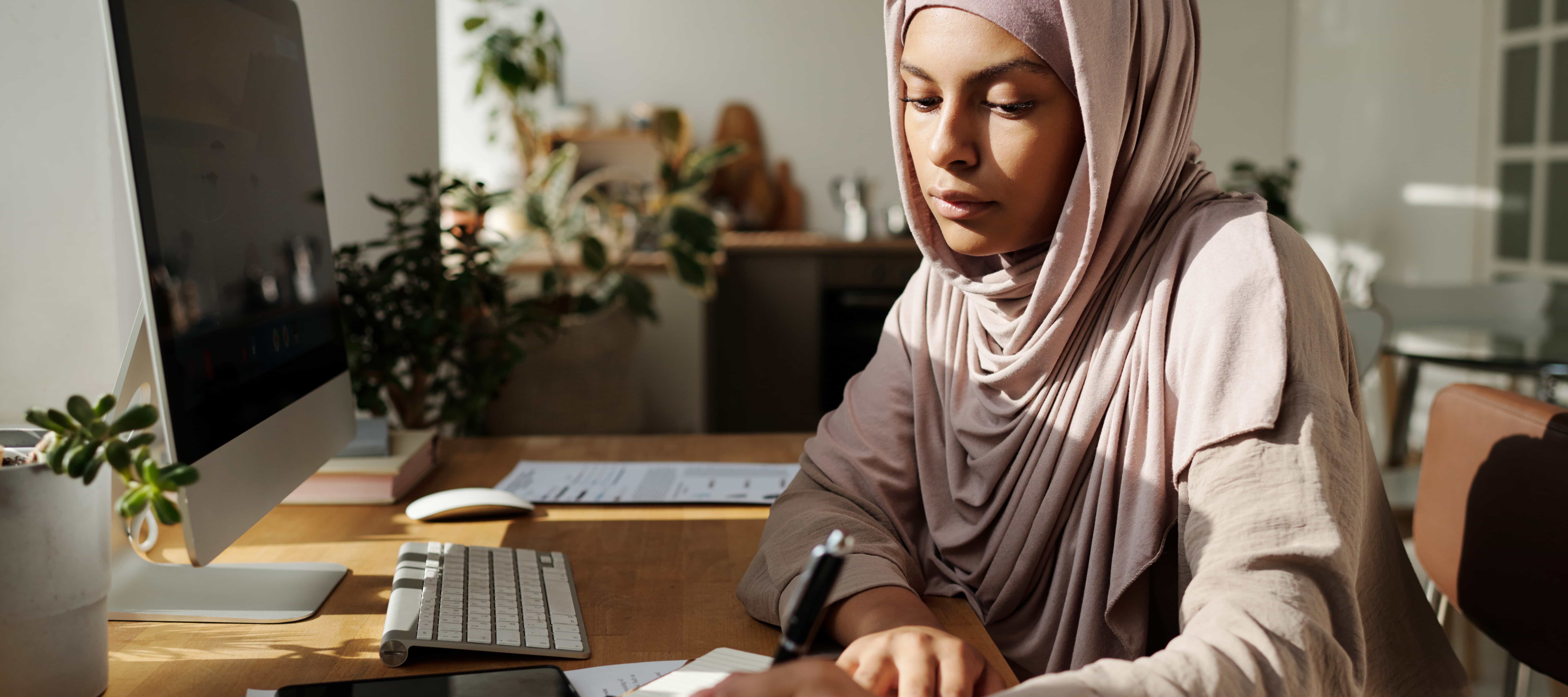 Young female employee reviewing financial documents at her computer desk