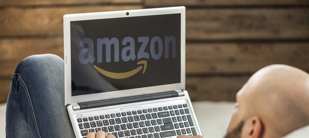 Photo of a man looking at his laptop screen, which is showing Amazon.