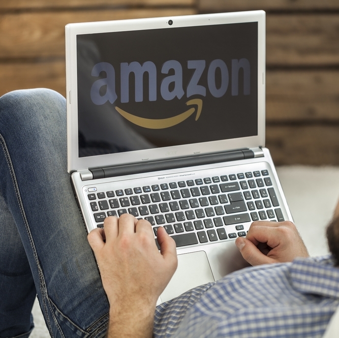 Photo of a man looking at his laptop screen, which is showing Amazon.