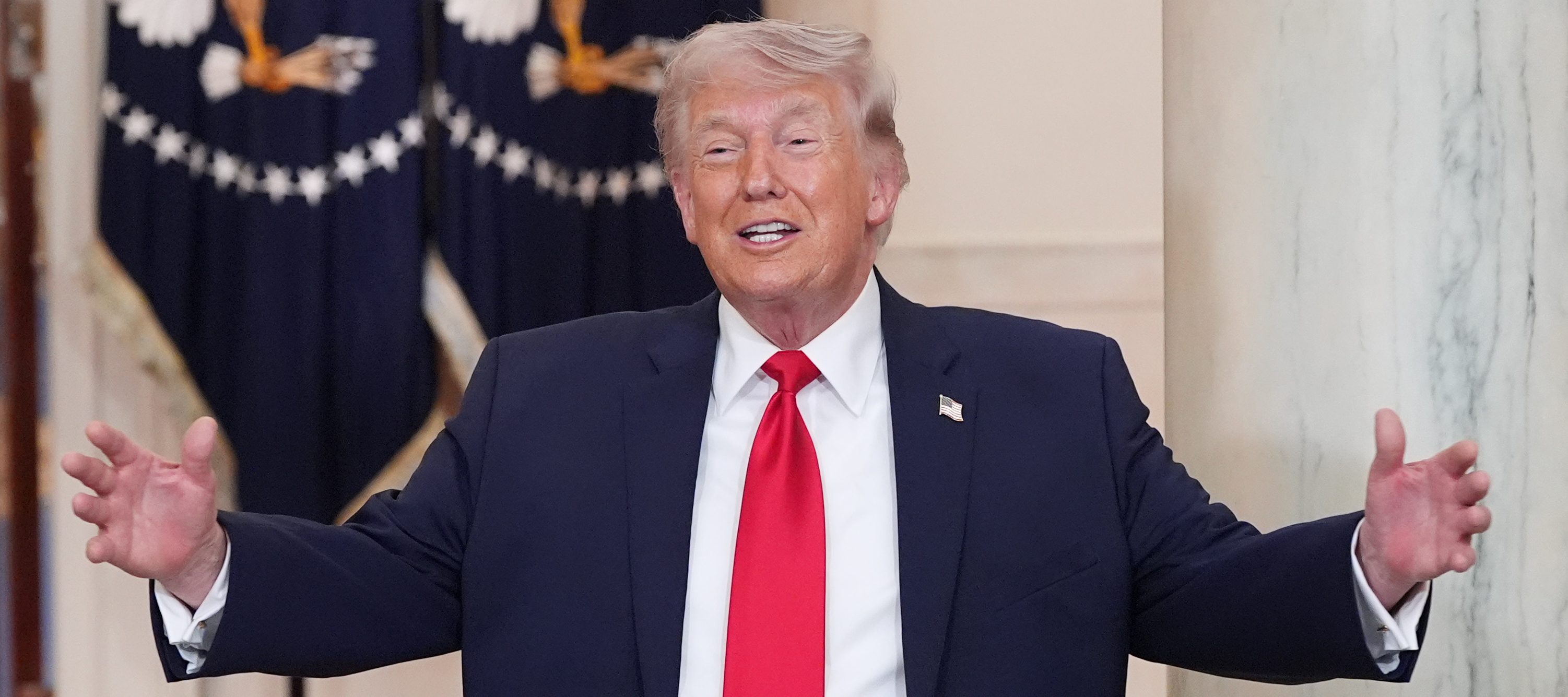 President Donald Trump stands with his arms spread wide and a smile on his face.