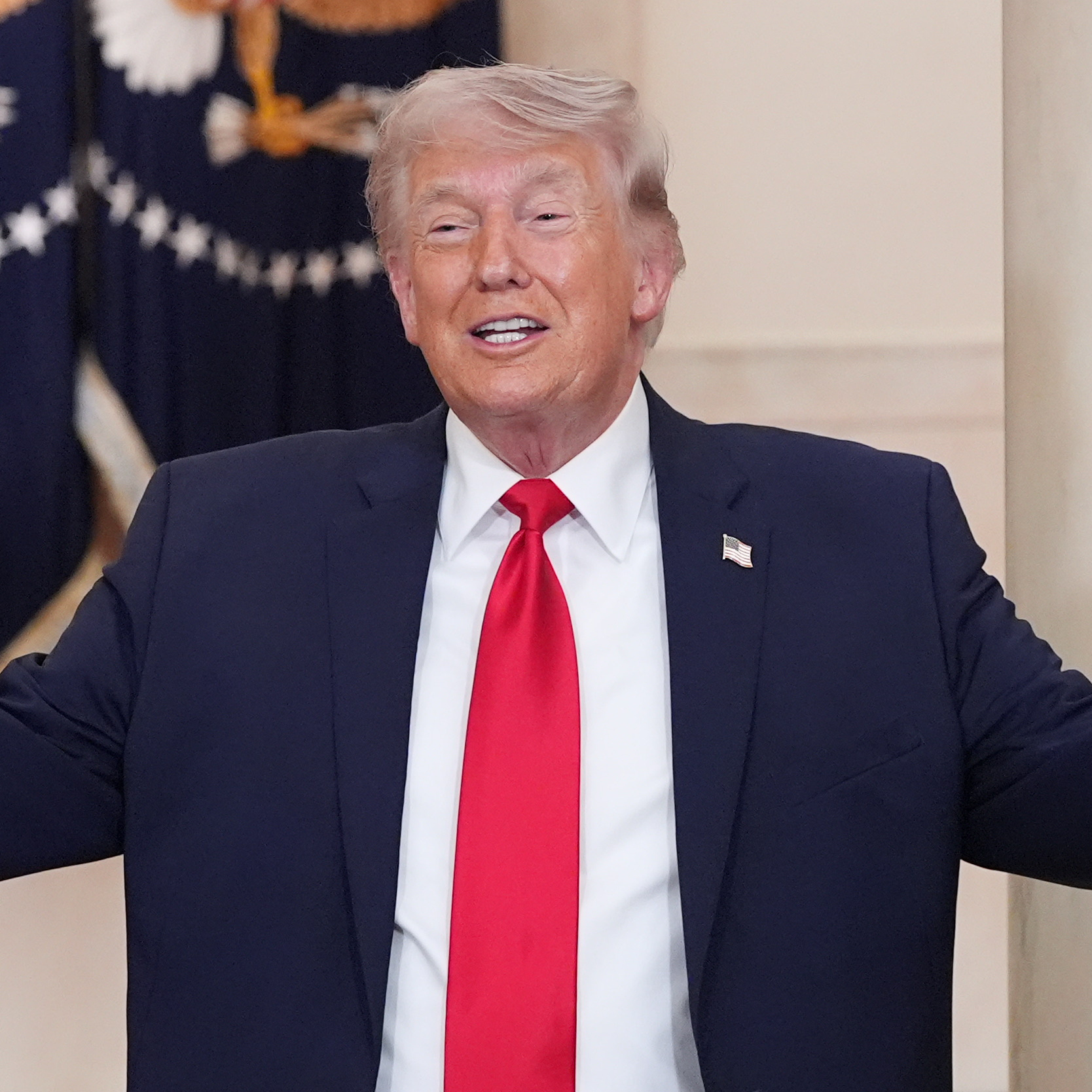President Donald Trump stands with his arms spread wide and a smile on his face.