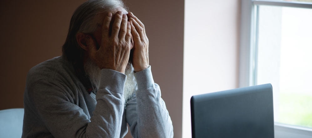 Distressed older man in front of laptop screen