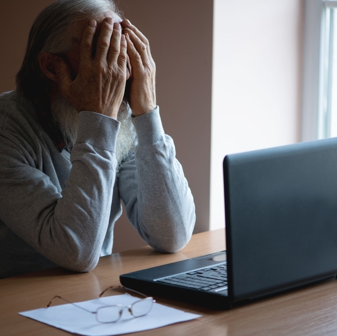 Distressed older man in front of laptop screen