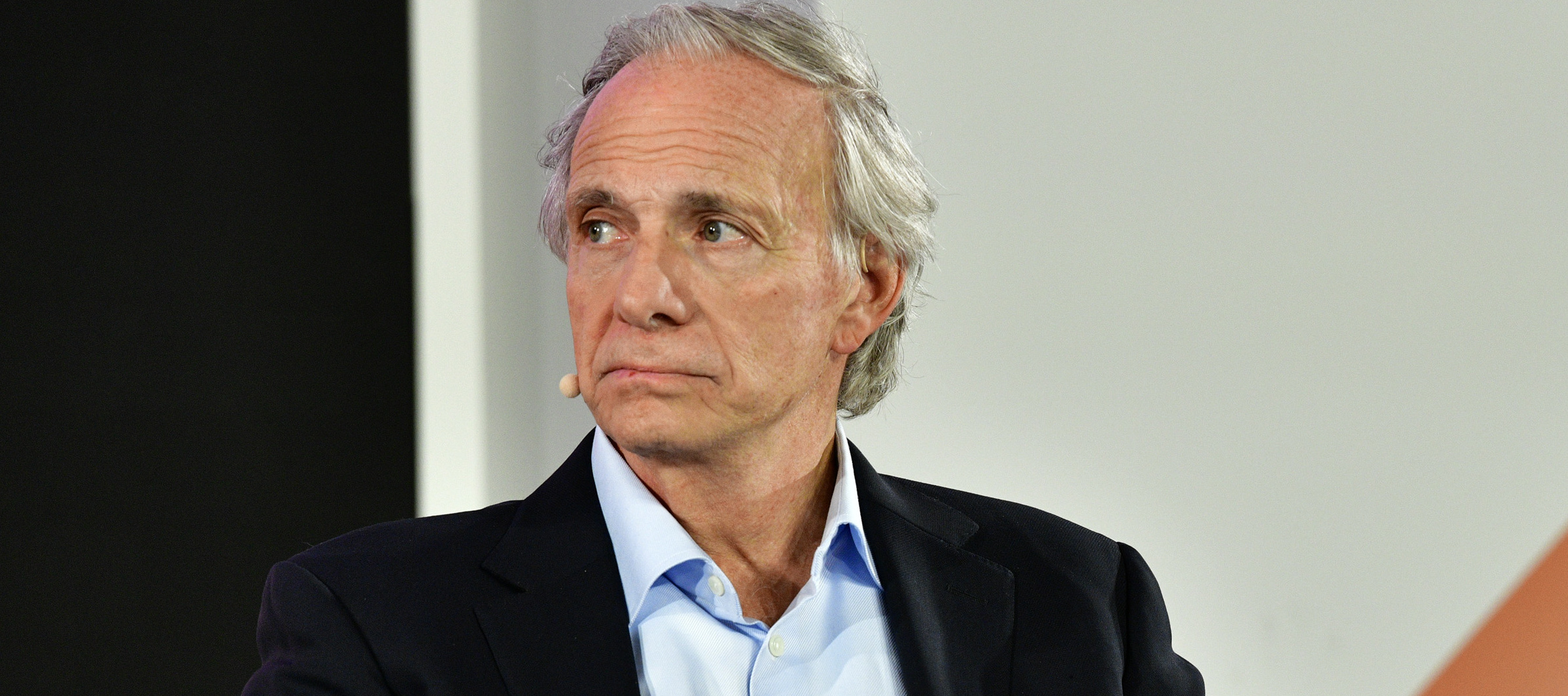 Ray Dalio sits in a plush chair for an interview, frowning intensely.