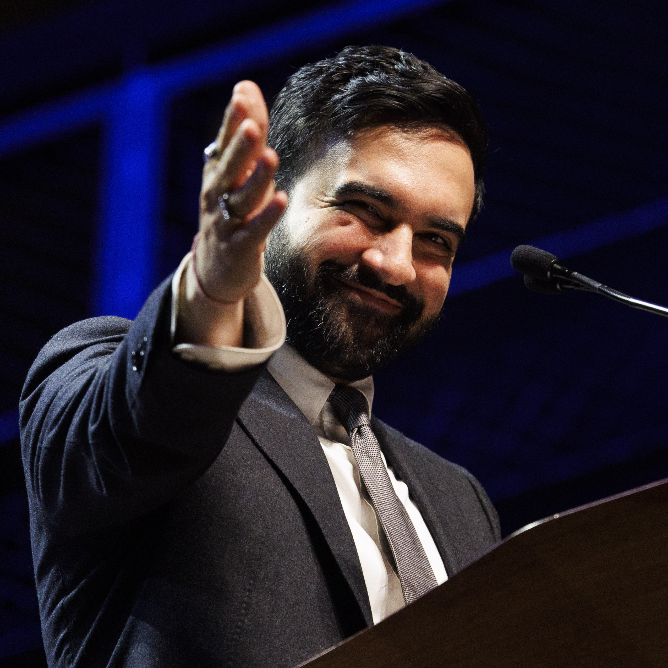 New York City Mayor Zohran Mamdani smiles at a podium while gesturing offstage.