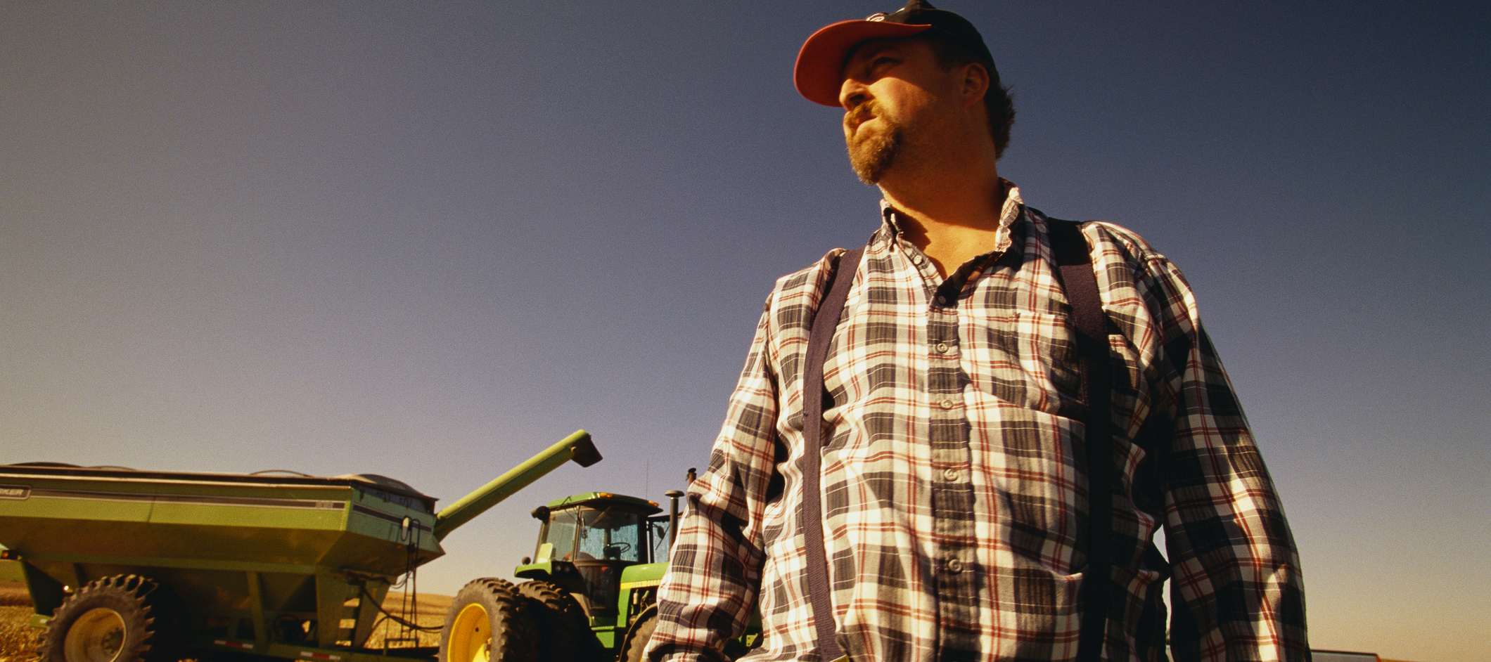 A photo of a farmer standing in a field in front of a tractor