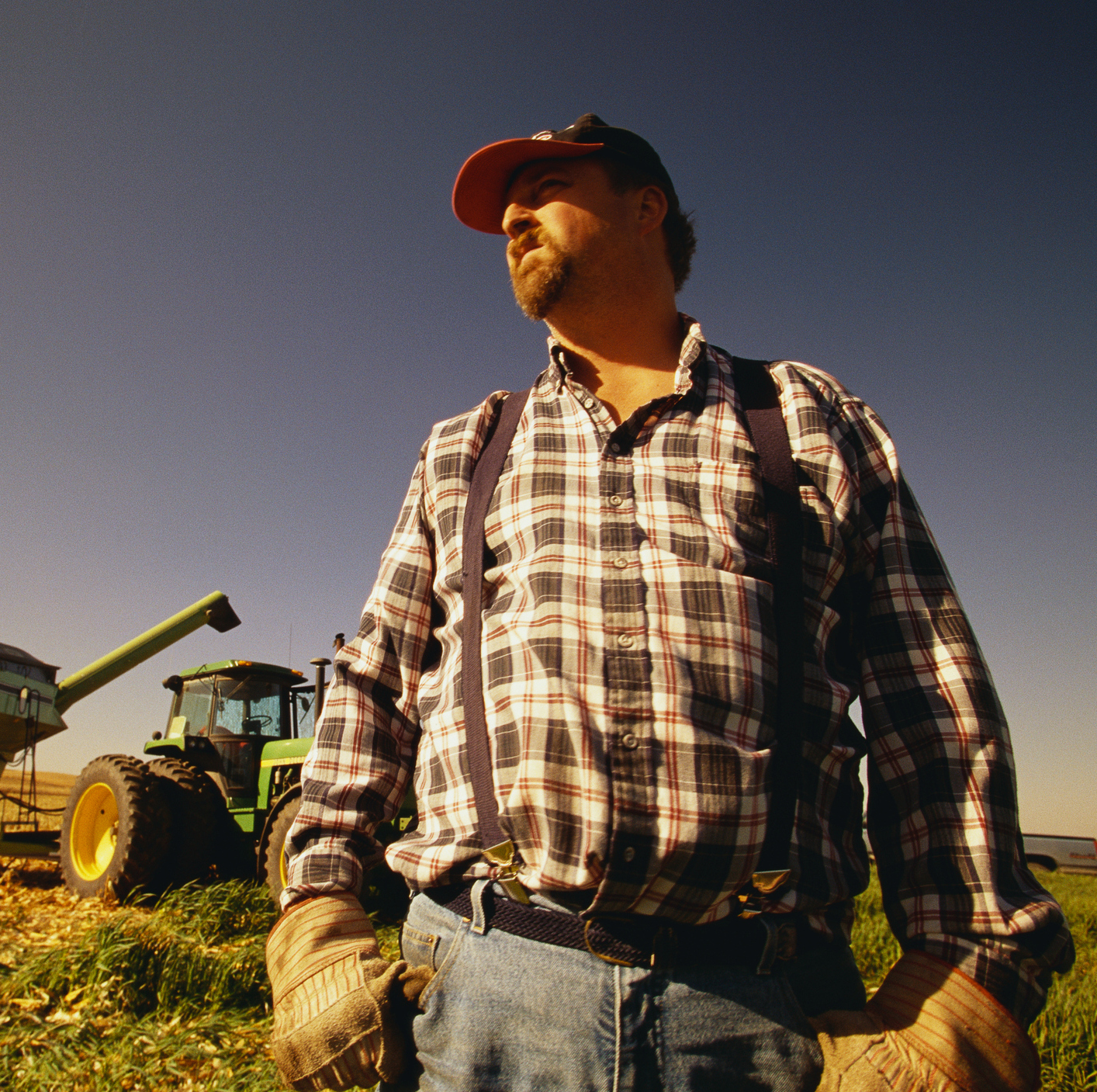 A photo of a farmer standing in a field in front of a tractor