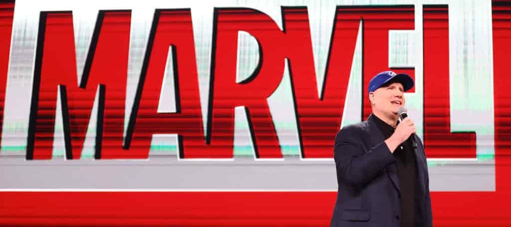 Kevin Feige, President of Marvel Studios, speaking on stage in front of a Marvel backdrop