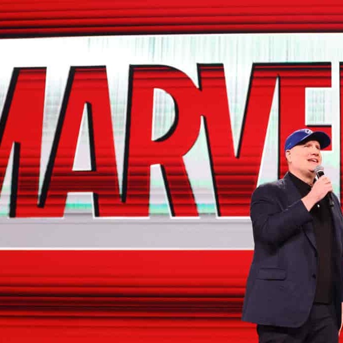 Kevin Feige, President of Marvel Studios, speaking on stage in front of a Marvel backdrop