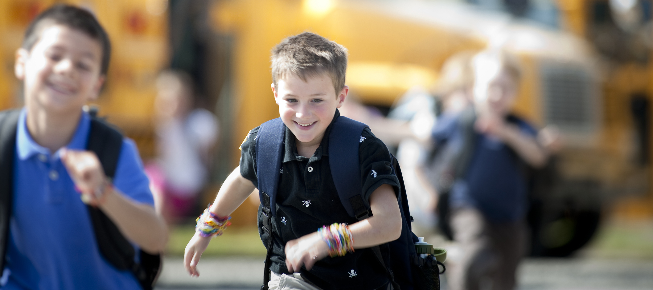 A photo of two male students cheerily running off a school bus