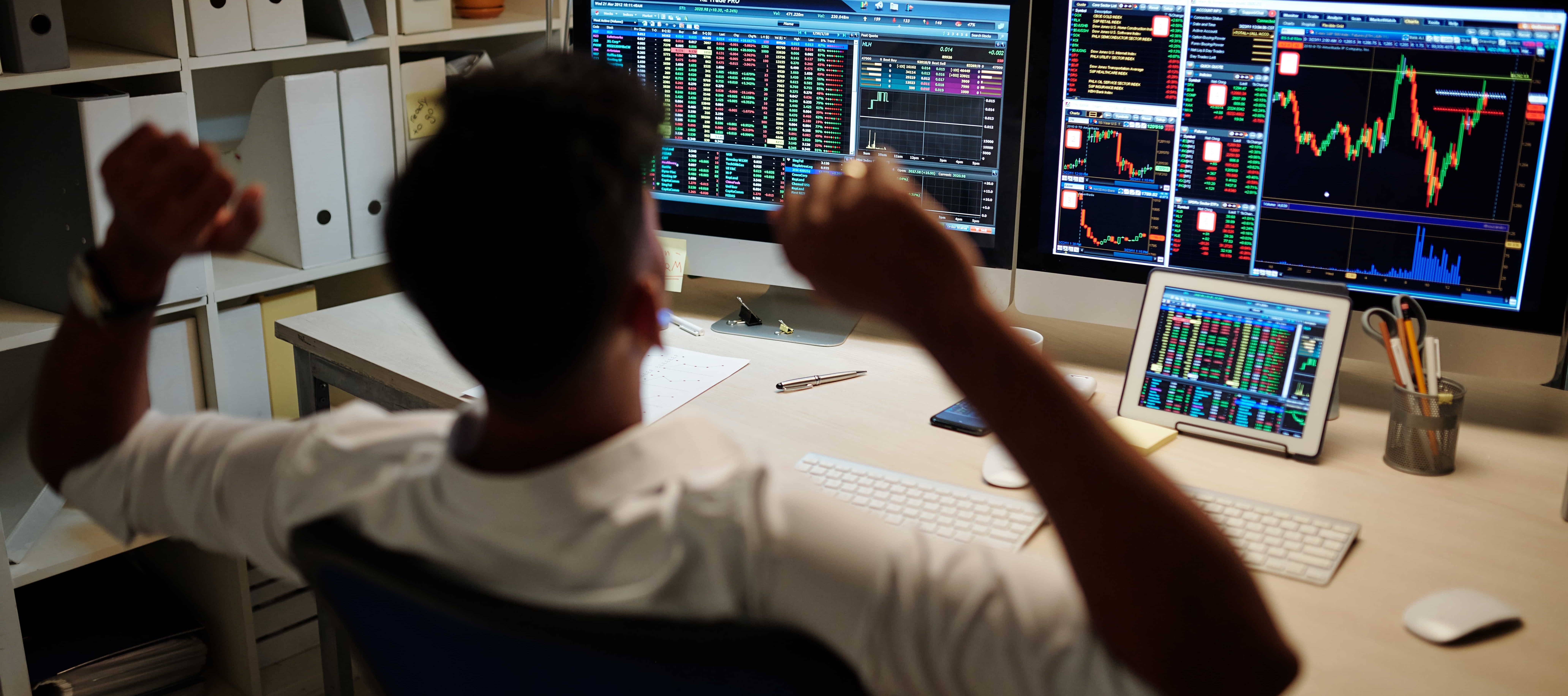 A photo of a day trader looking at investment market data on various screens
