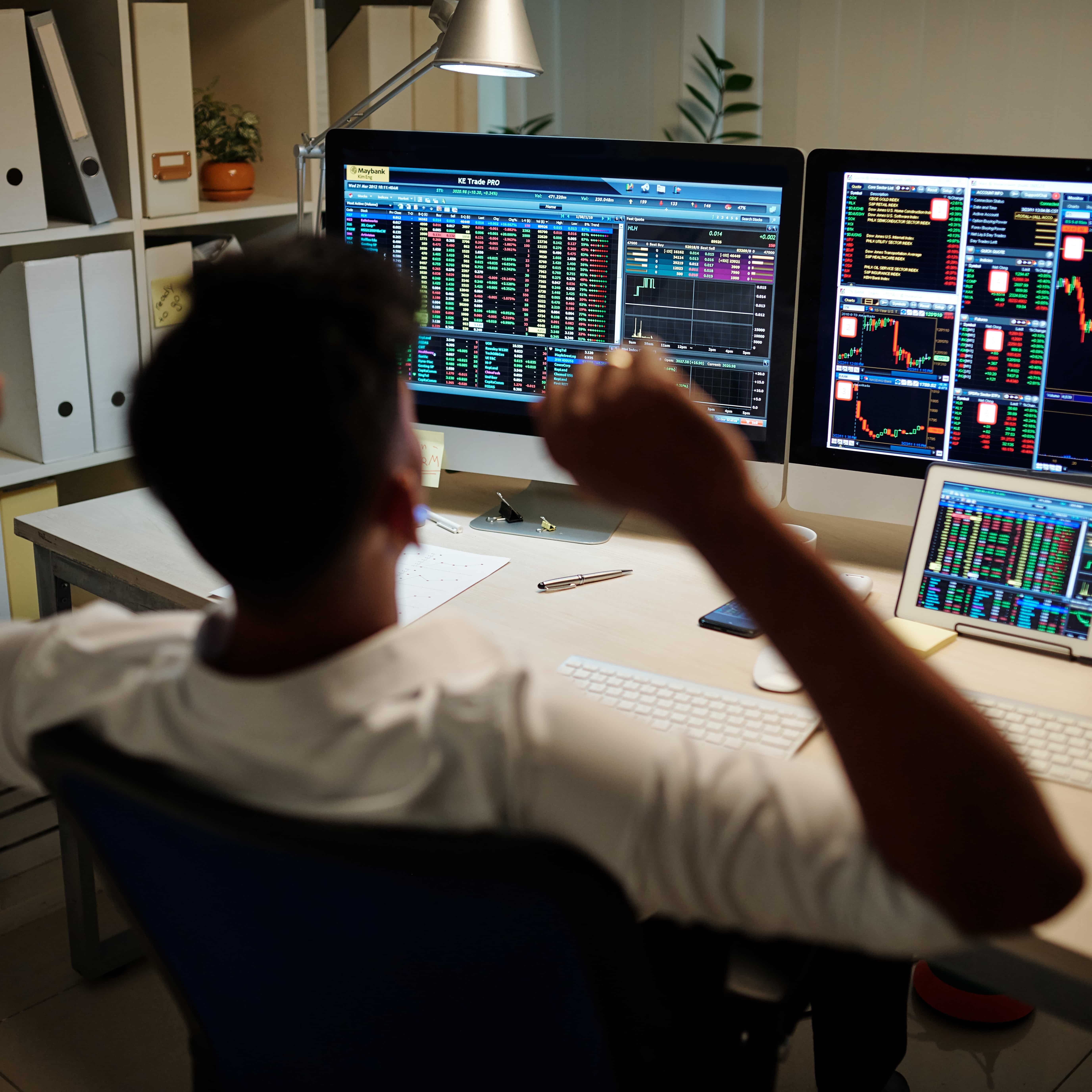 A photo of a day trader looking at investment market data on various screens