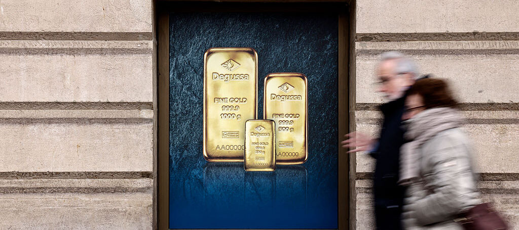 A woman and a man walking past a poster depicting investment gold bars on a gold dealer's window.