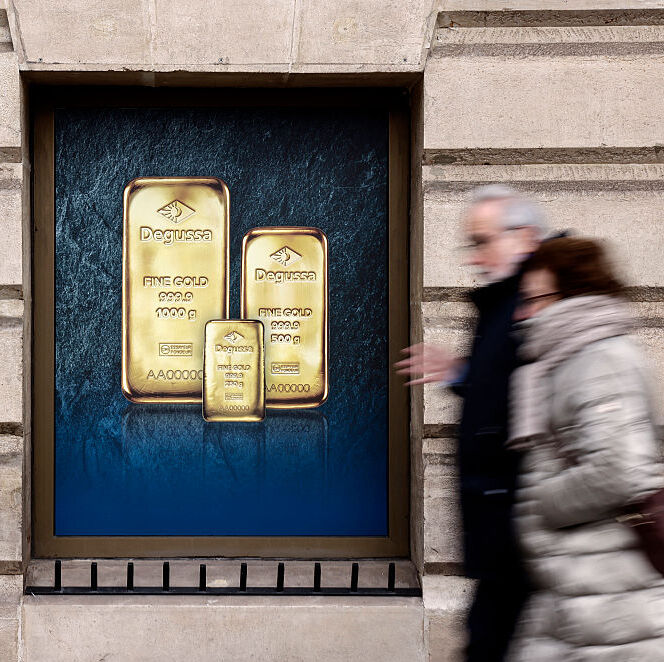 A woman and a man walking past a poster depicting investment gold bars on a gold dealer's window.