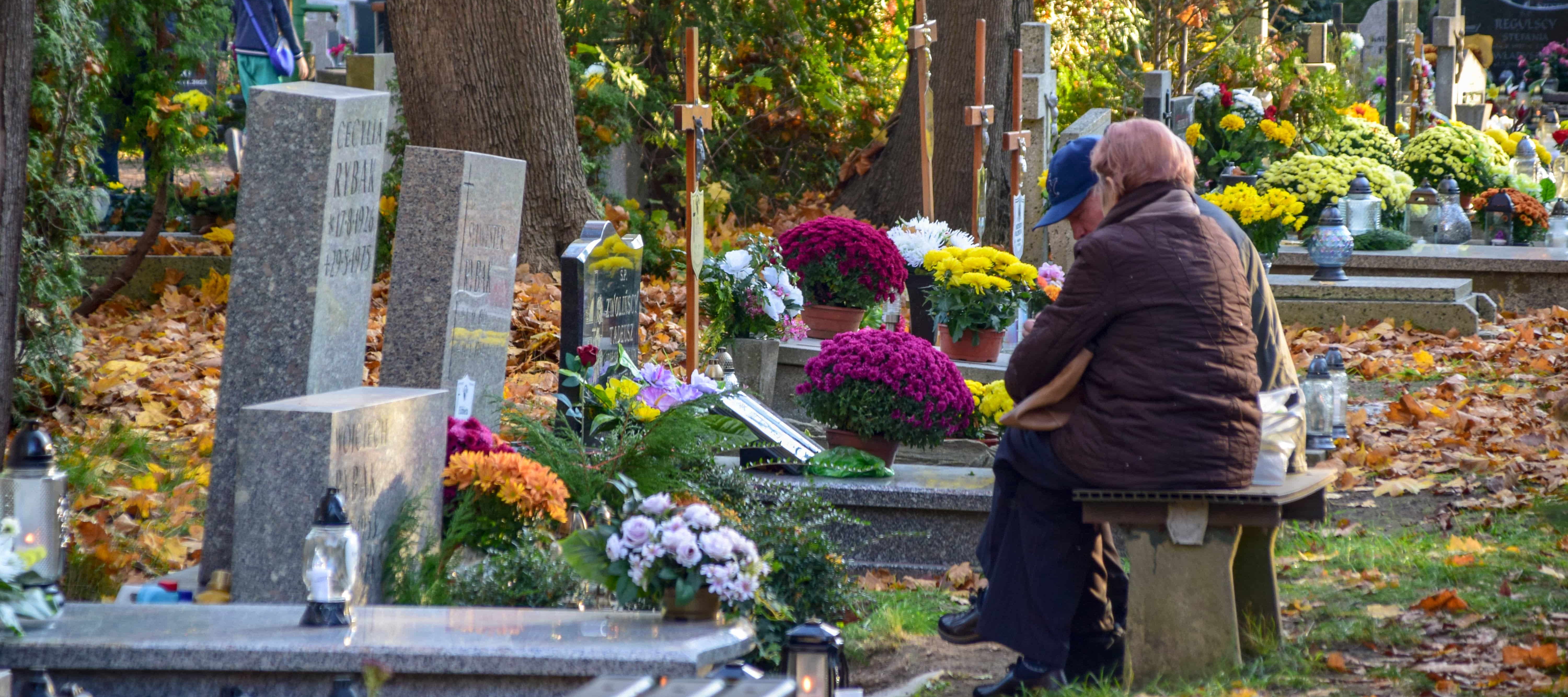 A photo of a grieving elderly couple sitting in a cemetery overlooking a gravesite