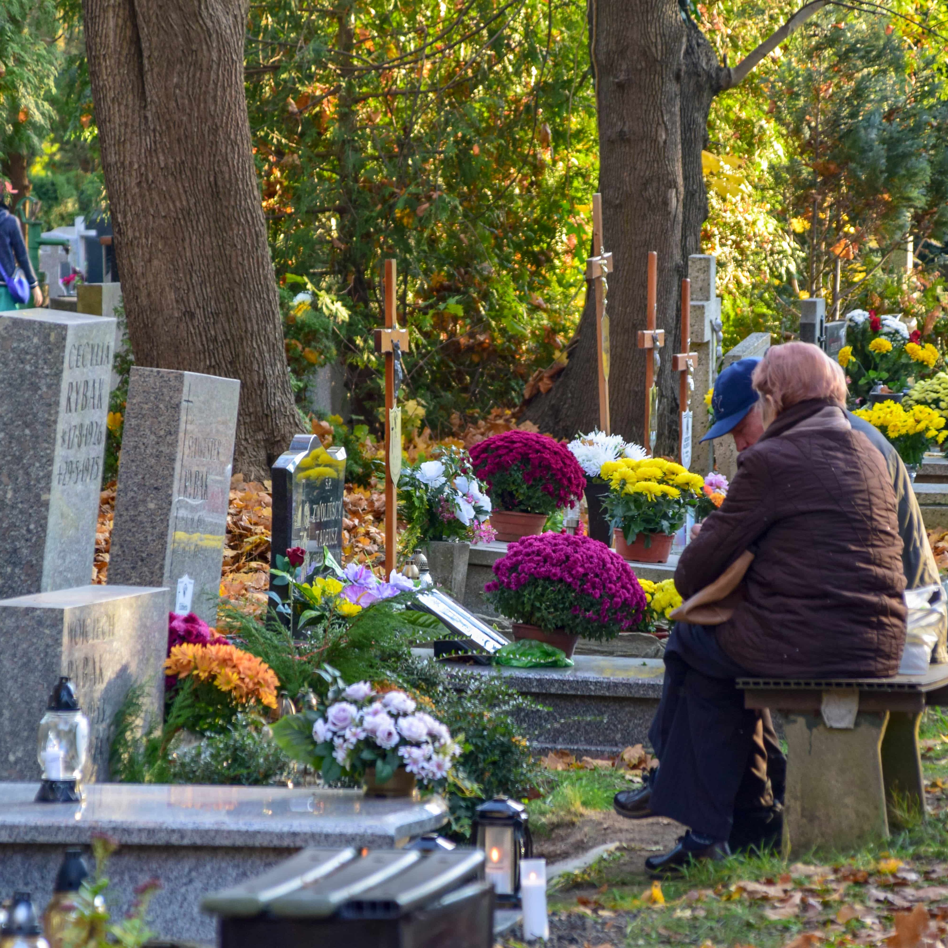 A photo of a grieving elderly couple sitting in a cemetery overlooking a gravesite