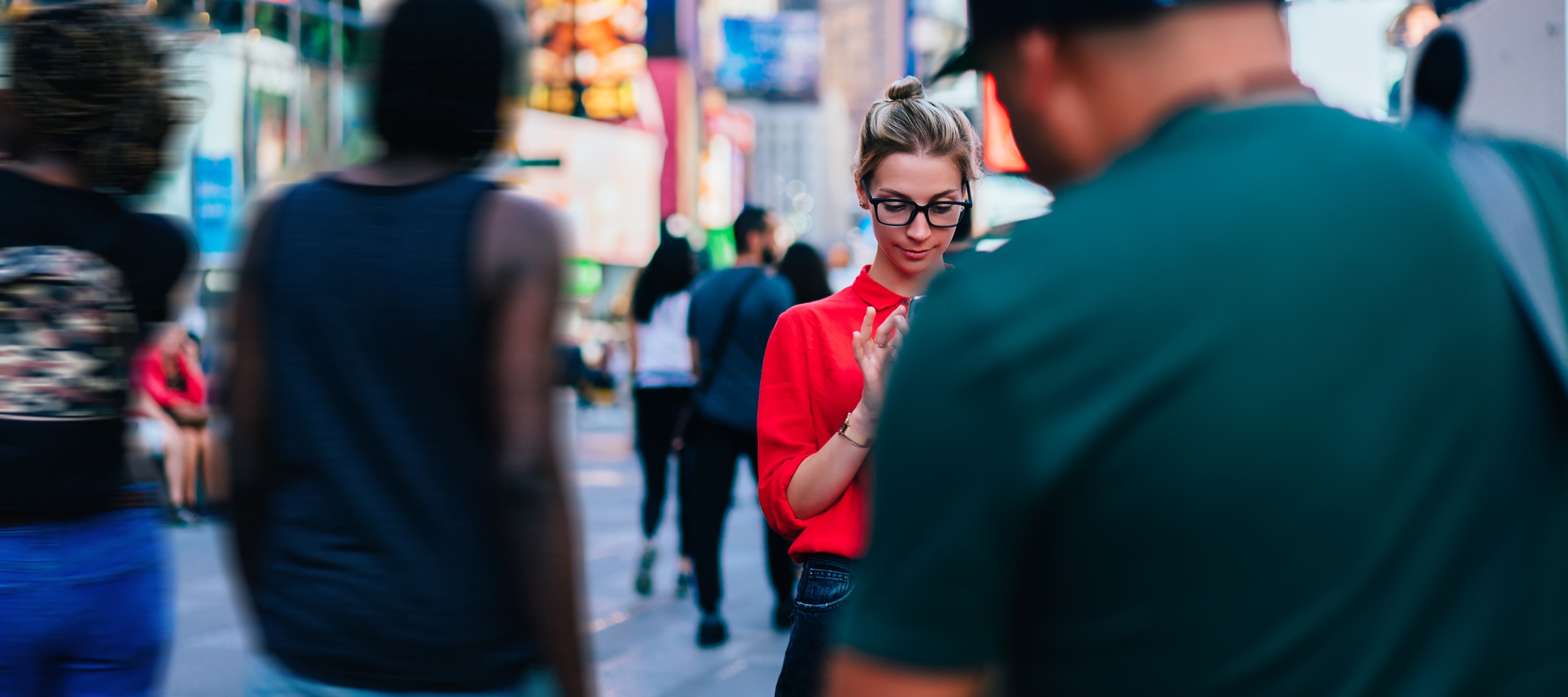 A woman stands in a crowded city looking at her phone.