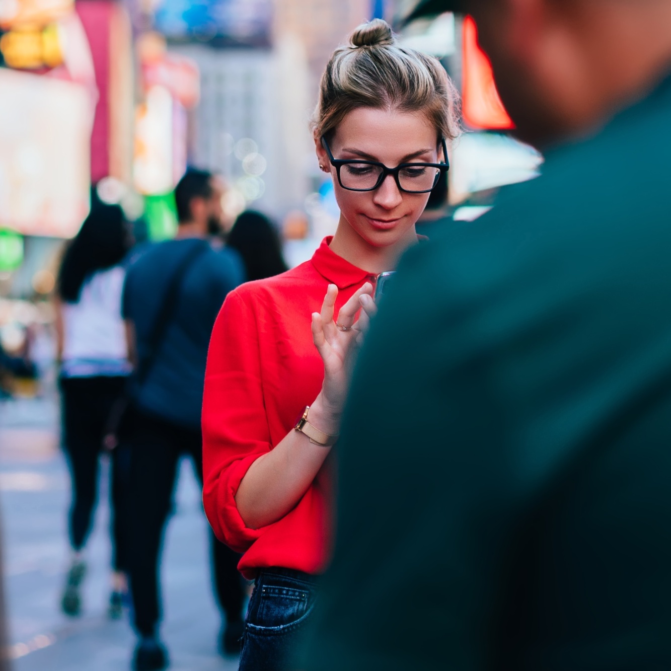 A woman stands in a crowded city looking at her phone.