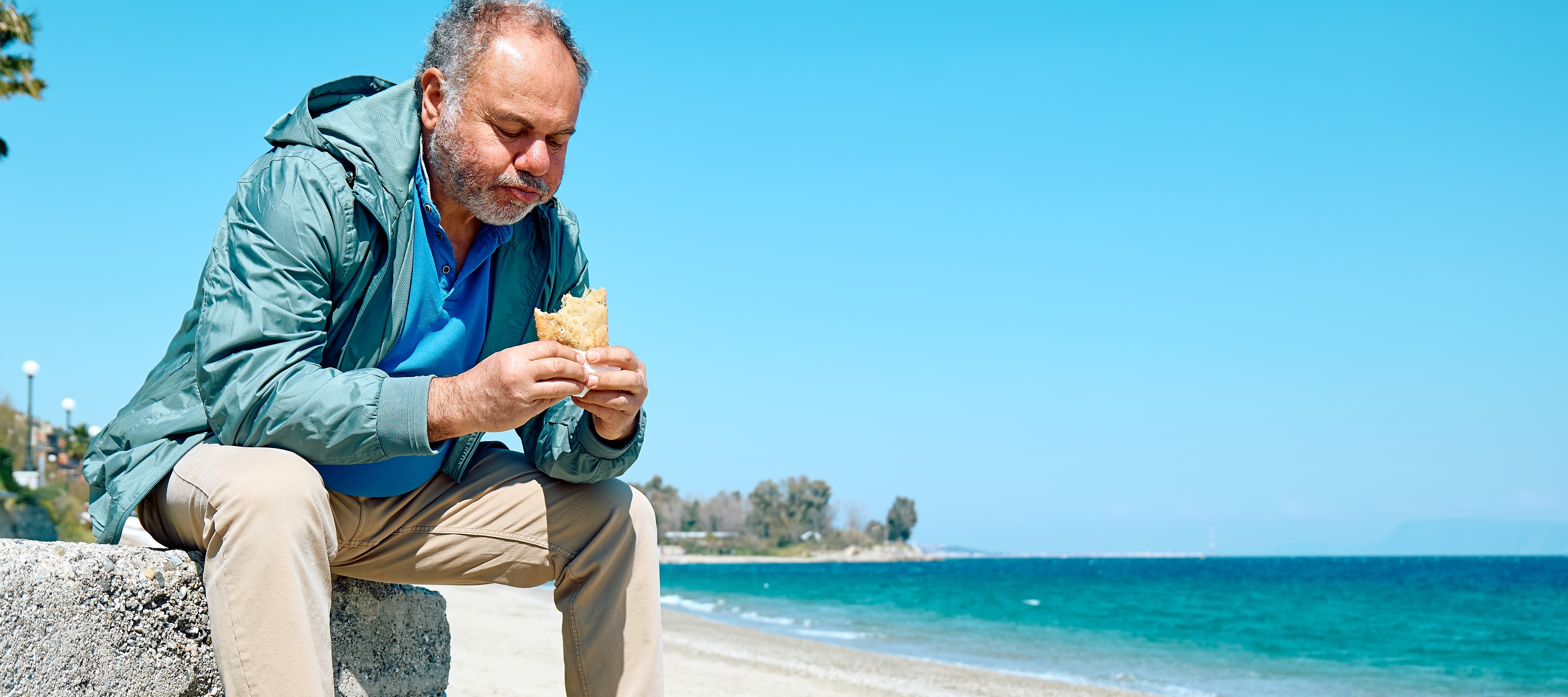 Bearded man eating on a park bench